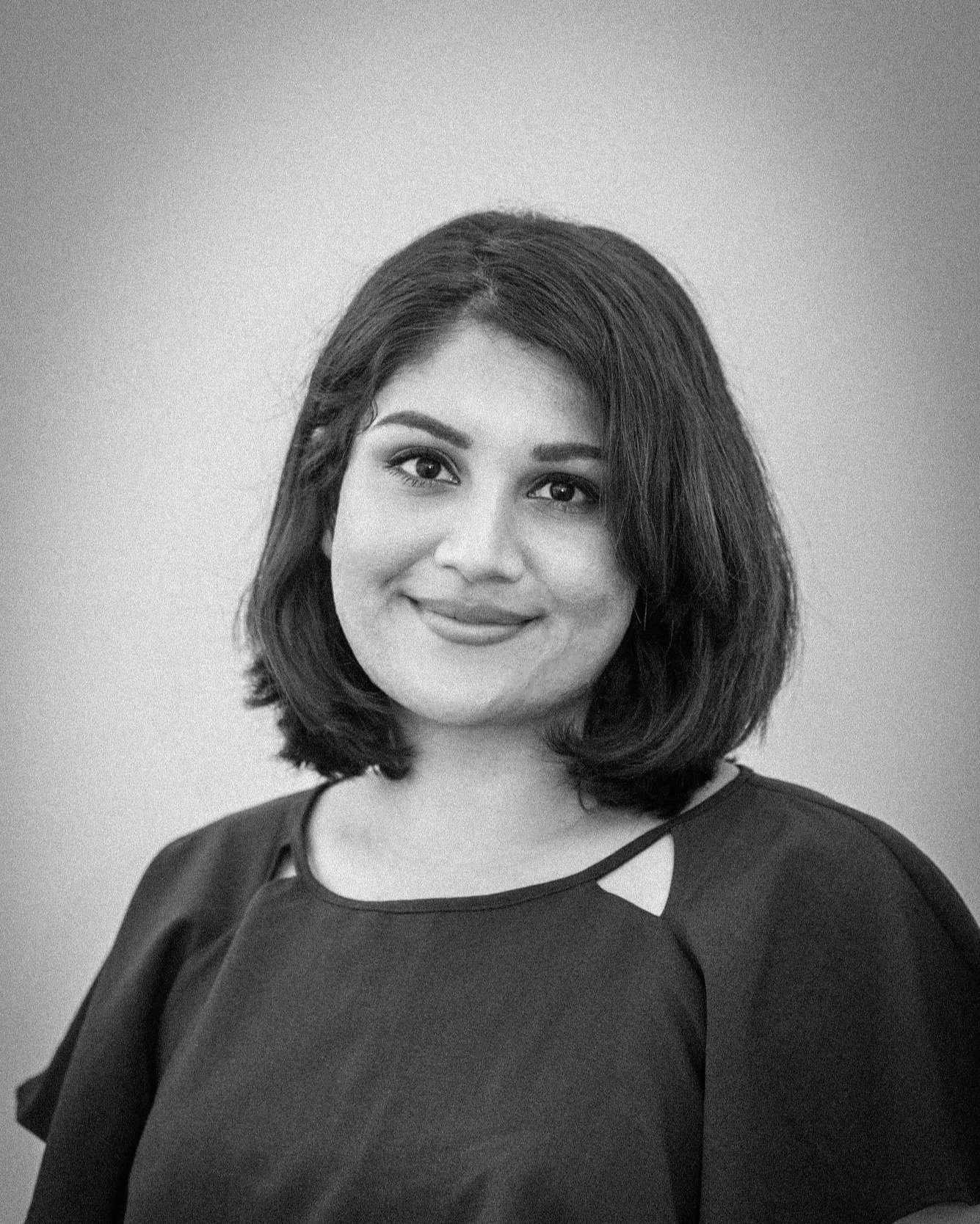 Black and white portrait of a woman with shoulder-length hair, wearing a dark top with cut-out shoulder details, smiling gently at the camera.