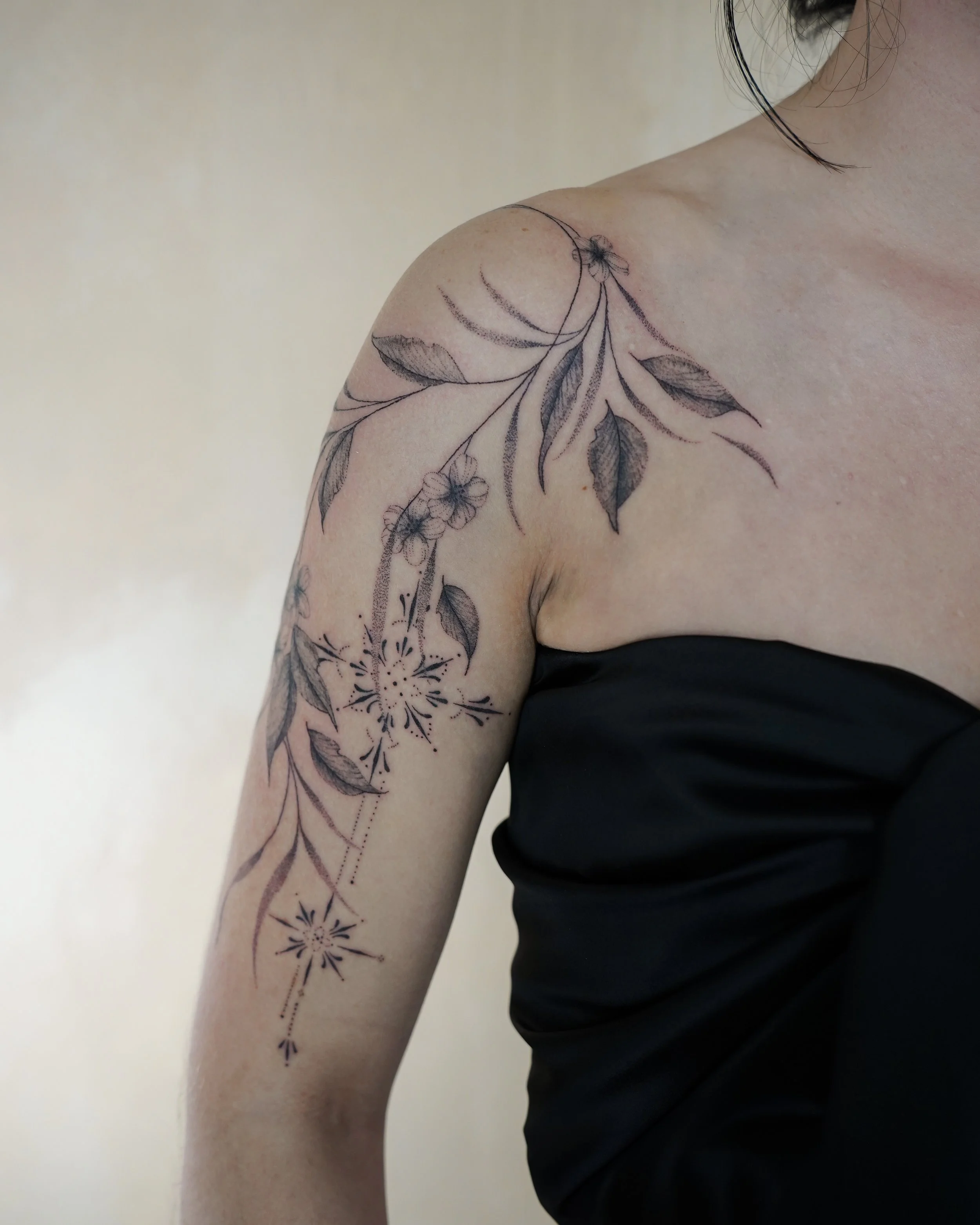 Tattoo of leaves and flowers on woman's upper arm and shoulder, with a black strapless top.