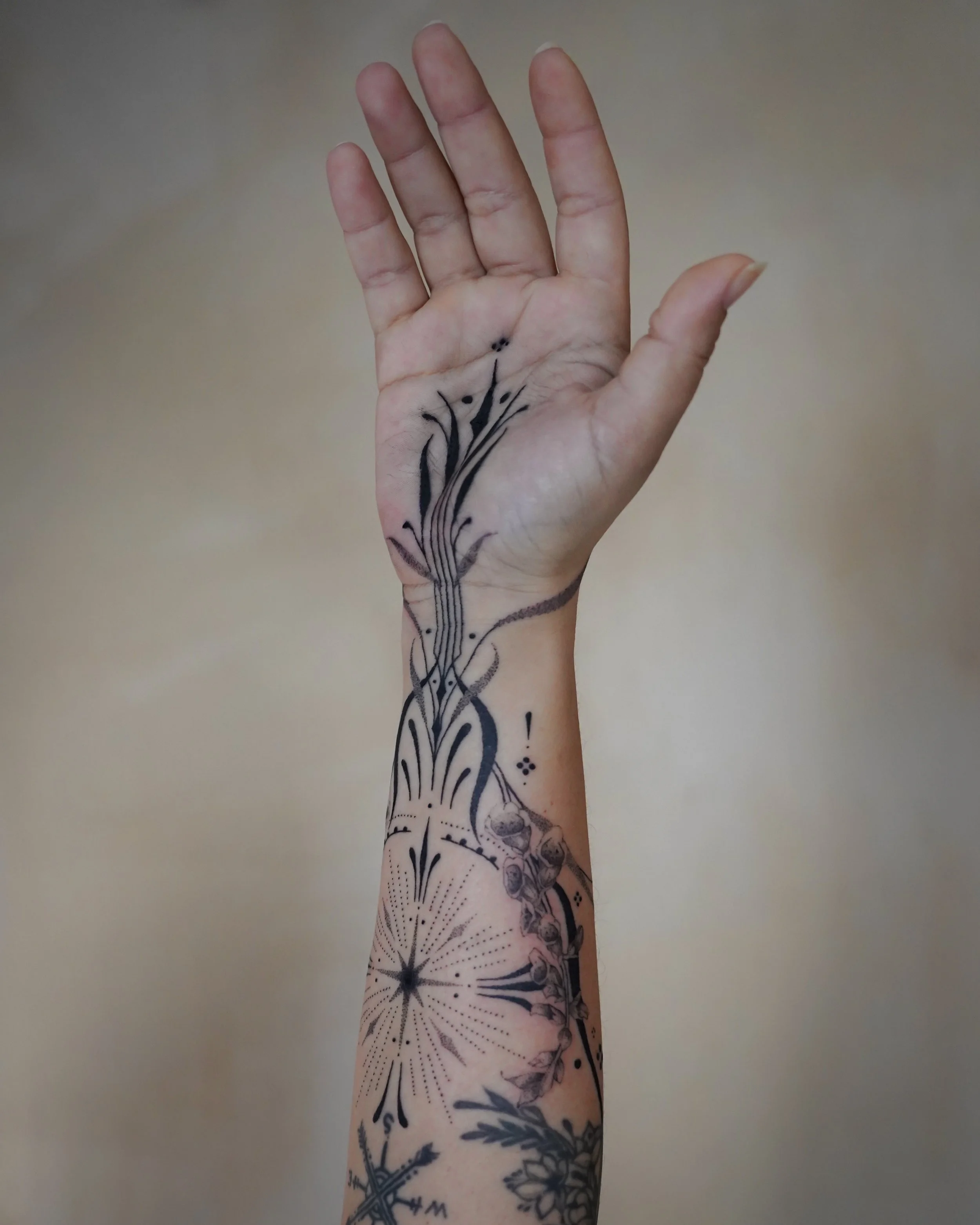 A person's arm raised upwards, displaying a black ink tattoo of abstract, flowing lines and dots, with additional floral designs on the forearm.