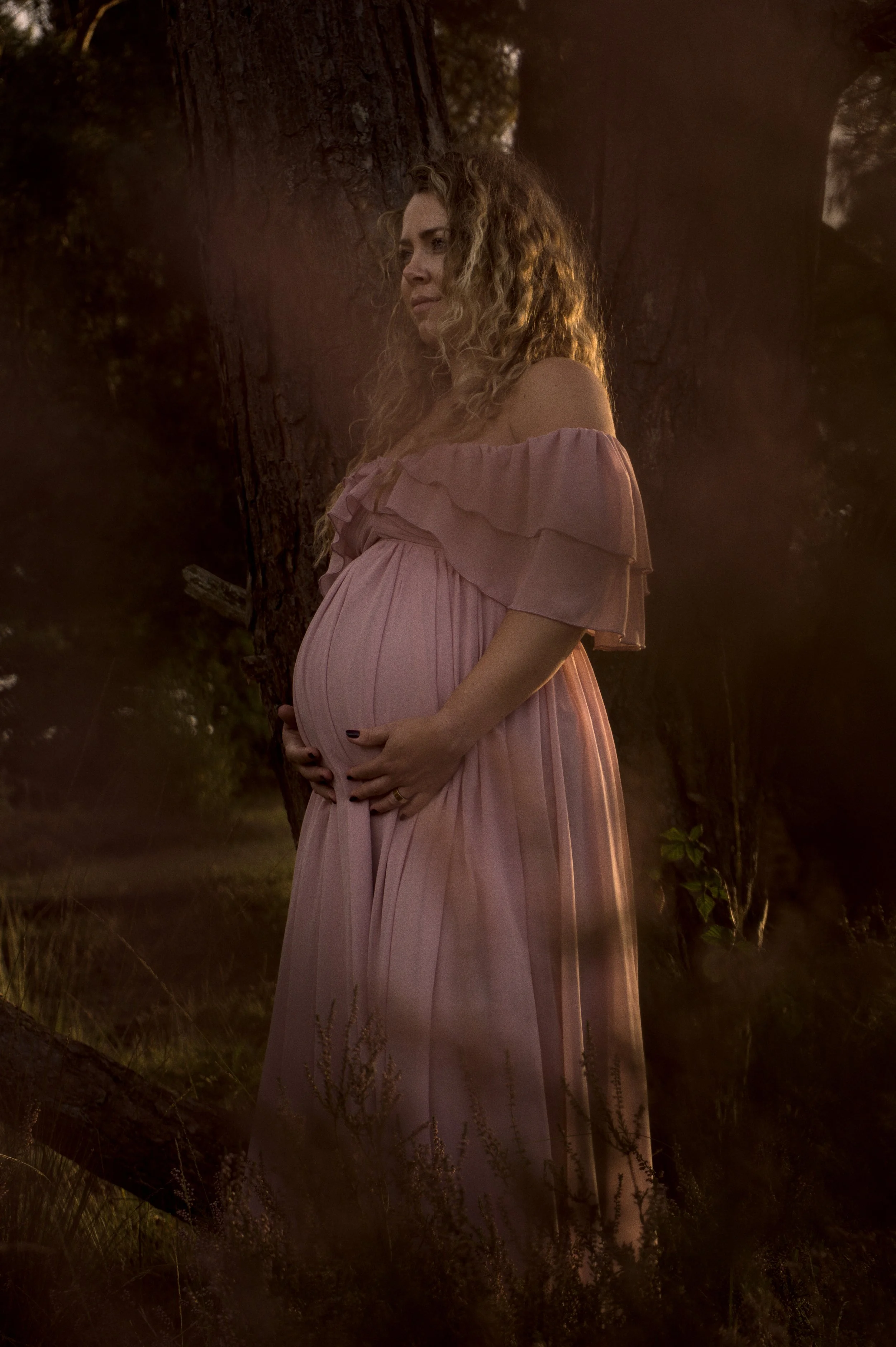 Zwangerschapsfotografie: zwangere vrouw in roze jurk in het bos bij laatste licht
