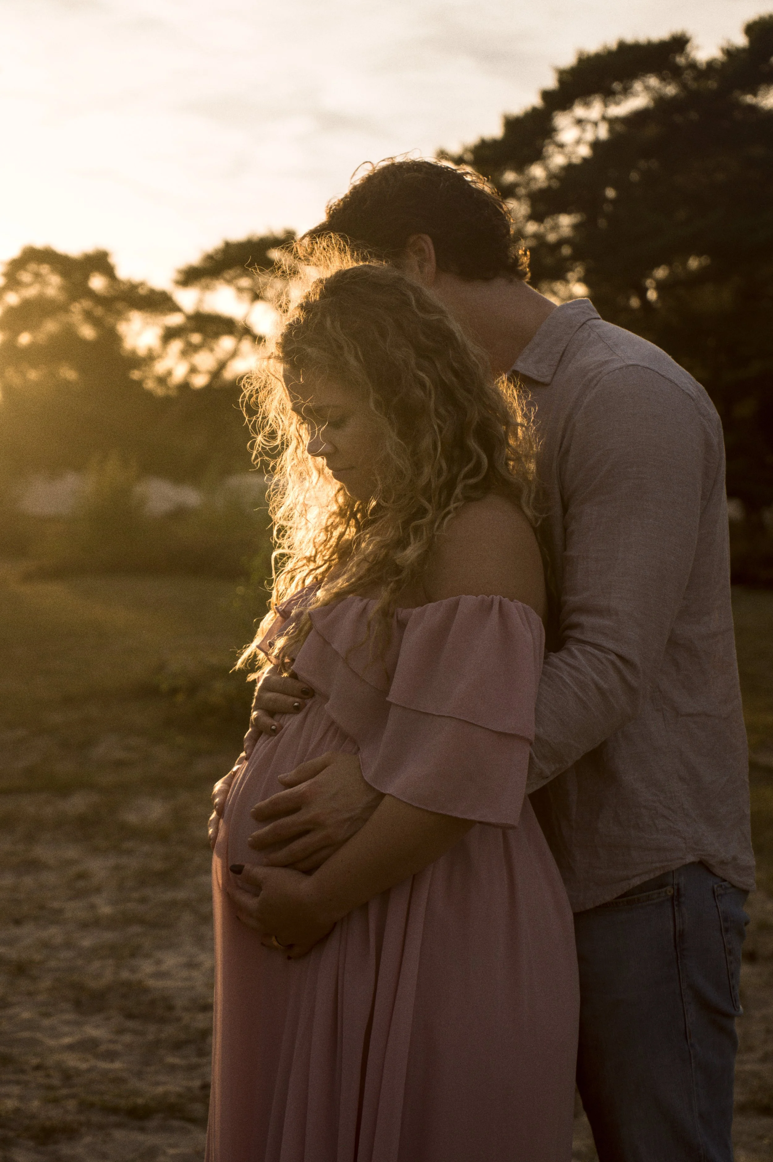 Zwangerschapsfotografie: aanstaande ouders in gouden tegenlicht, handen op de buik