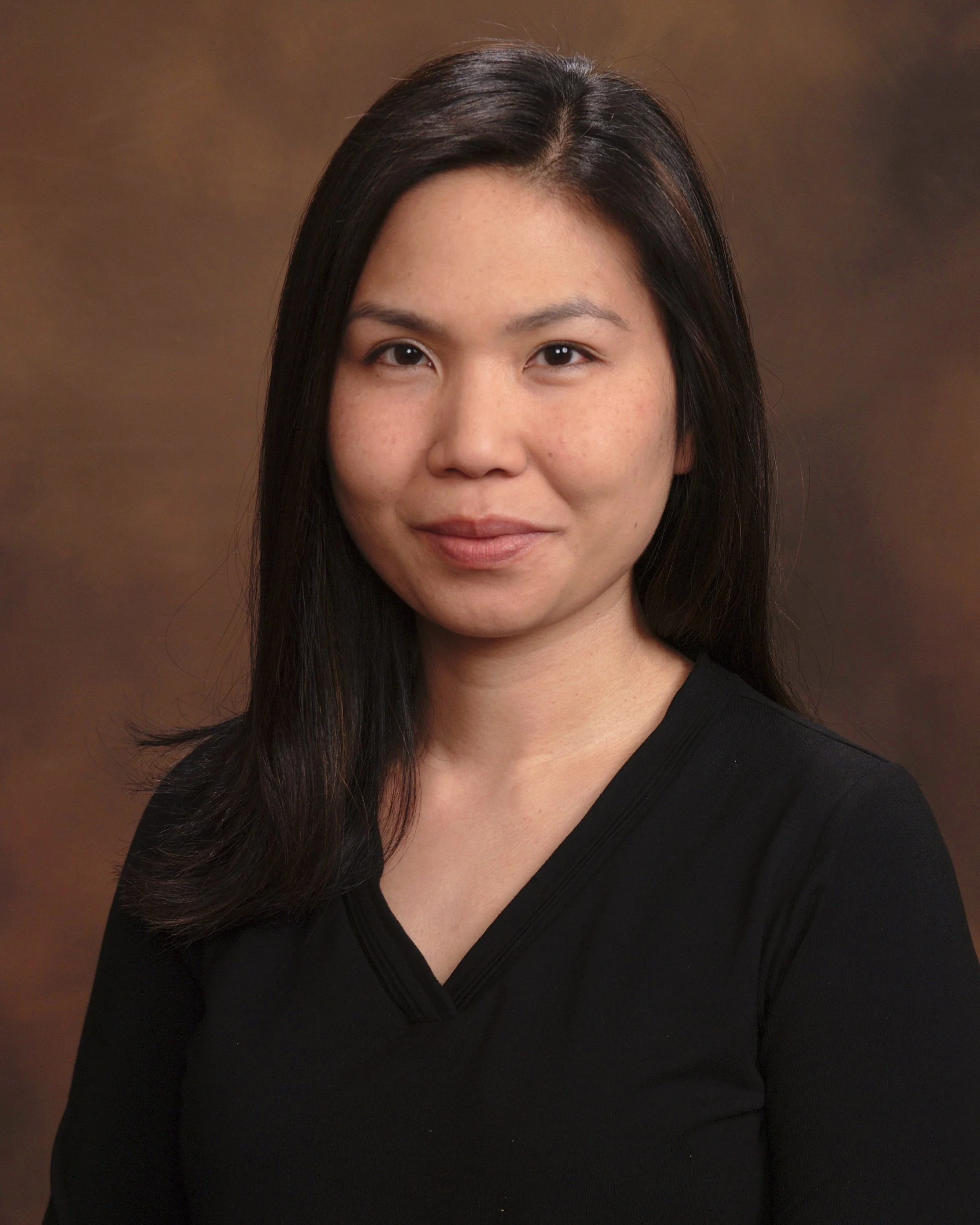 Portrait of a woman with black hair, wearing a black top, on a brown background.