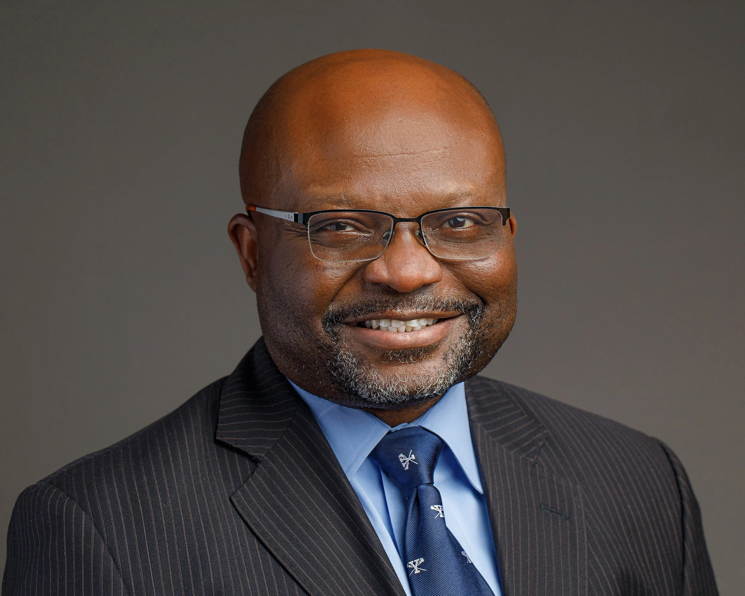 Smiling man in glasses wearing a suit and tie against a gray background.