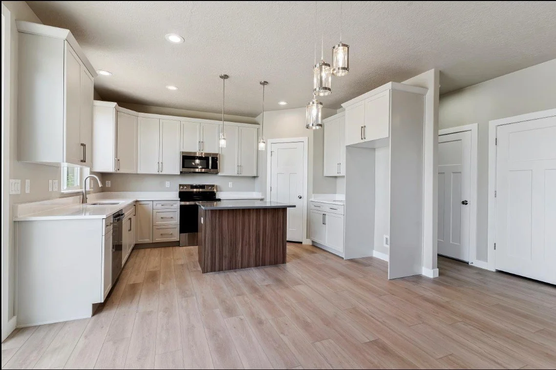 Modern kitchen with white cabinets, stainless steel appliances, a small island with a wood finish, and pendant lighting. Riverdale, utah