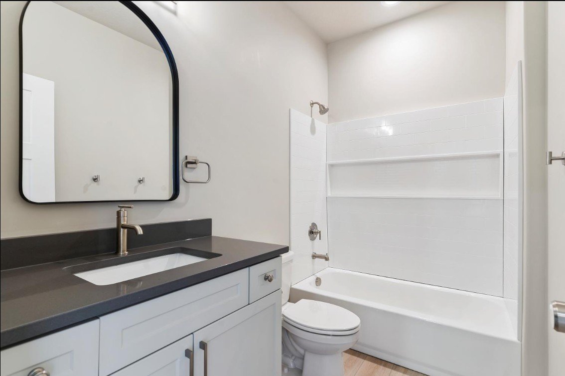 Bathroom with a white vanity, black countertop, square undermount sink, large mirror, toilet, and a bathtub with a shower. Davis County, Clearfield, Utah