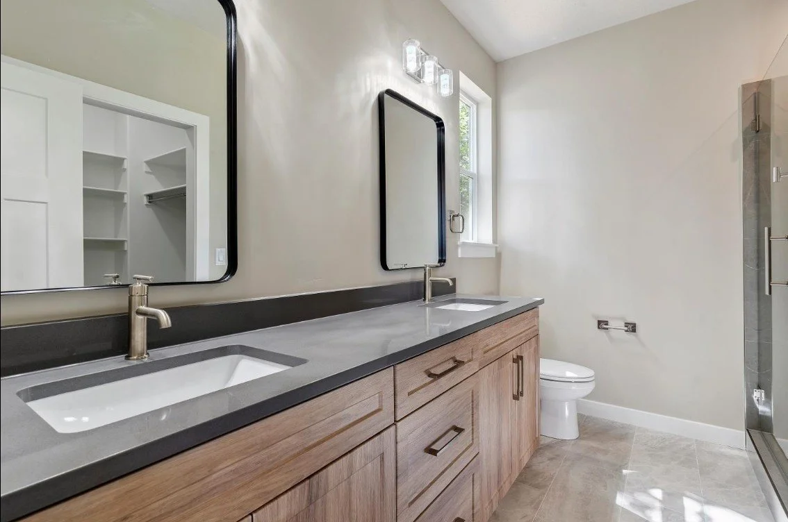 Modern bathroom with dual sinks, wooden vanity, large mirrors, and a walk-in shower with glass door. Hooper utah