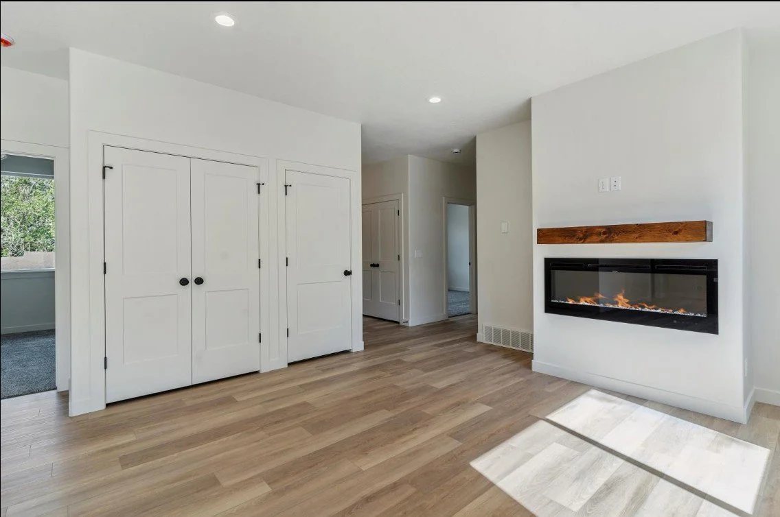 Empty living room with white walls, wooden floor, built-in electric fireplace on the right, and closet with double doors on the left. custom home builder in northern utah