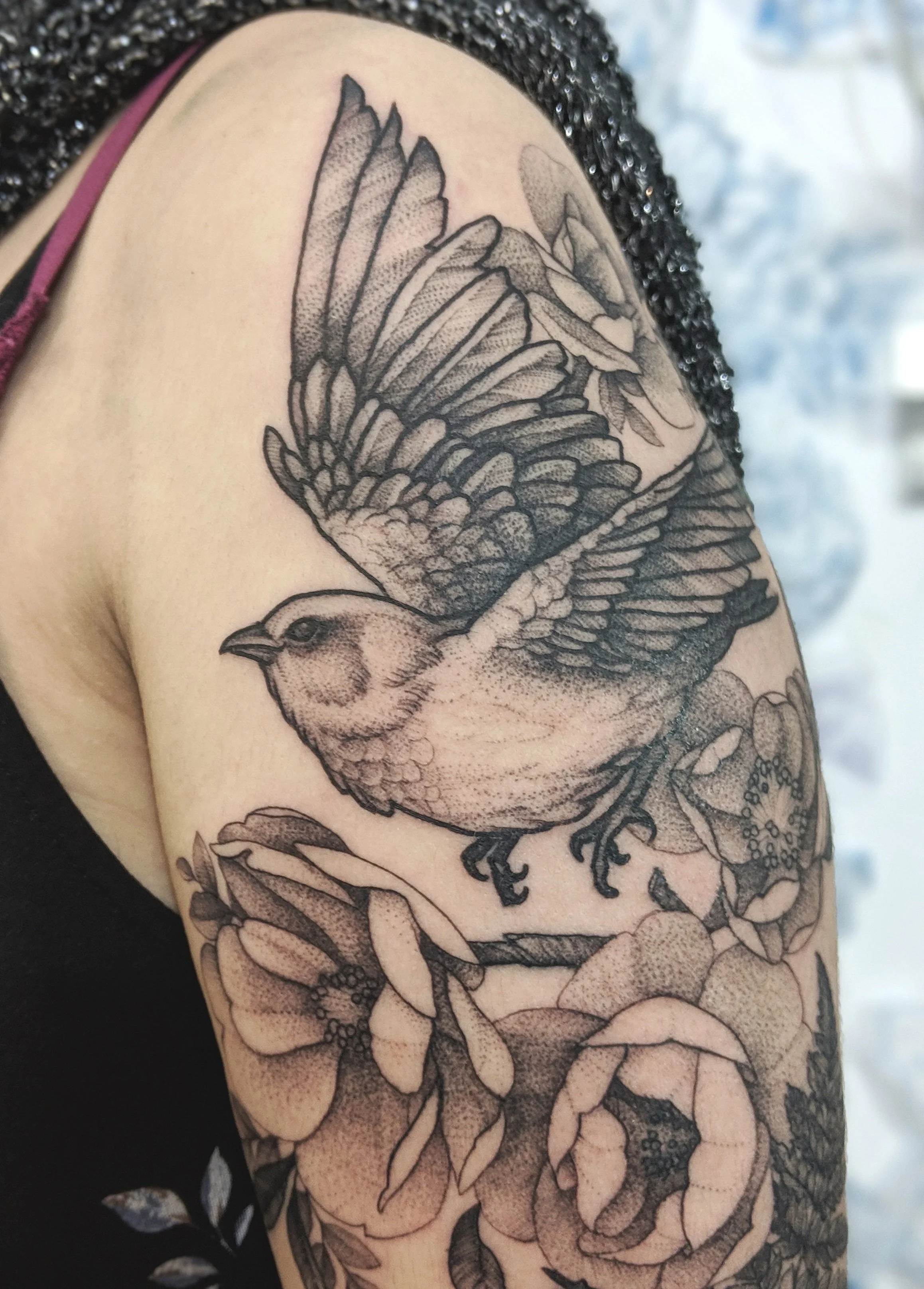 Tatouage d'un oiseau en plein vol avec des fleurs sur un bras.jpg