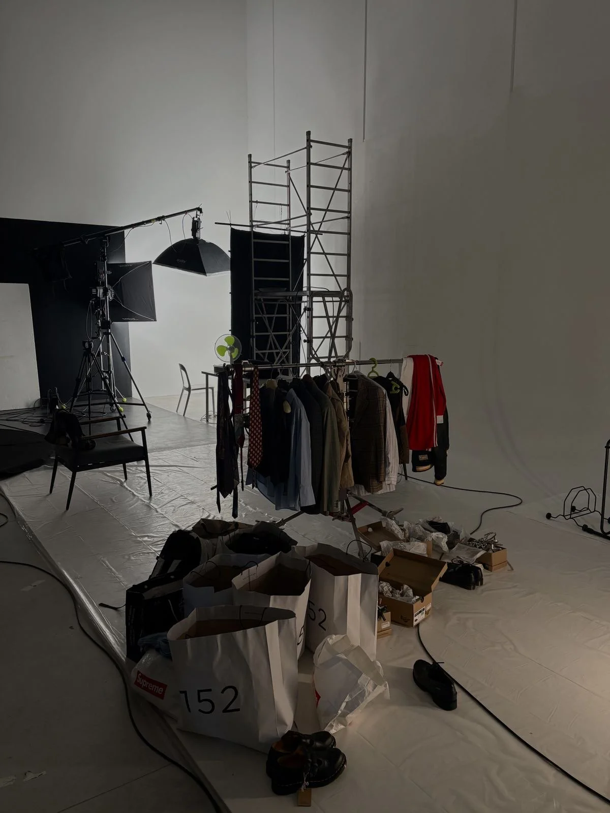 Photography studio with clothing rack, bags, shoes, and lighting equipment against a white backdrop.