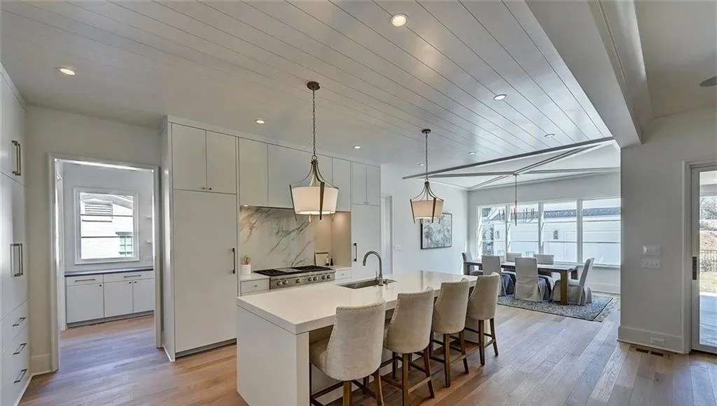 Open-concept kitchen and dining area with white cabinetry, island with chairs, hardwood floors, and large windows