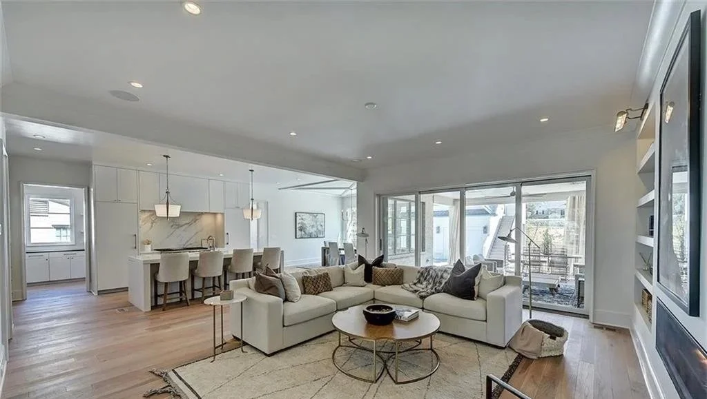 Open-concept living room and kitchen with white walls, eames-style dining chairs, large window, and sliding doors leading to a balcony.