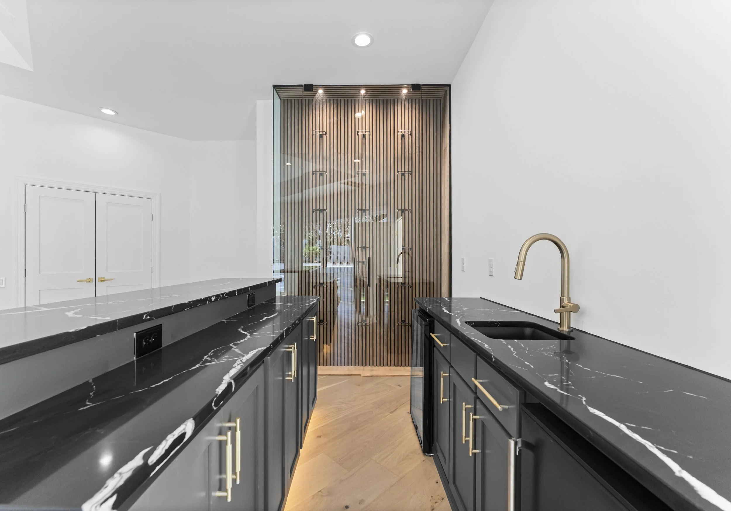 Modern kitchen with black marble countertops, matching cabinets with gold handles, a gold faucet, and a wooden slatted divider at the back.