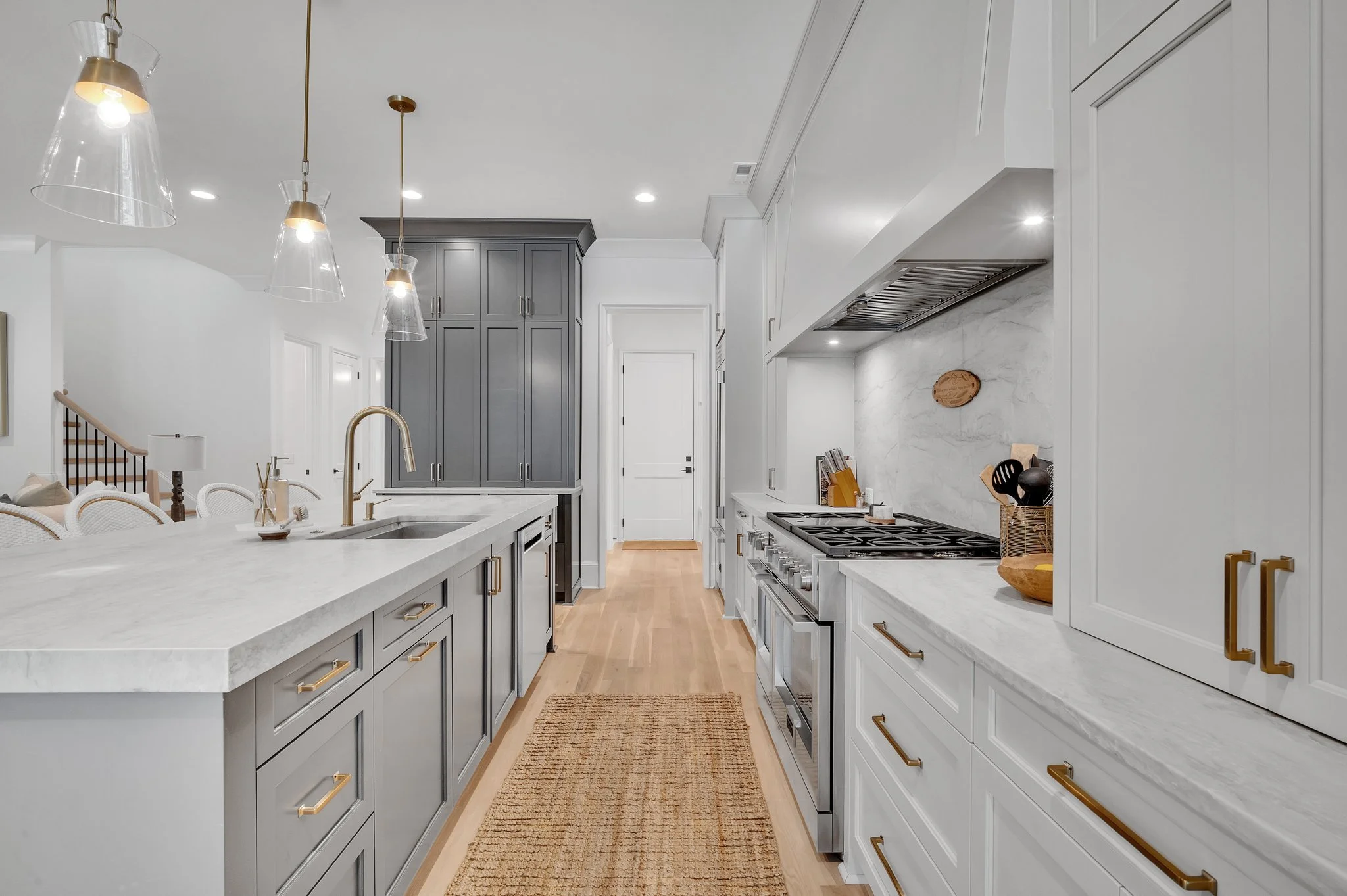 Modern kitchen with white and gray cabinetry, marble countertops, gold hardware, a gas stove, and pendant lighting.