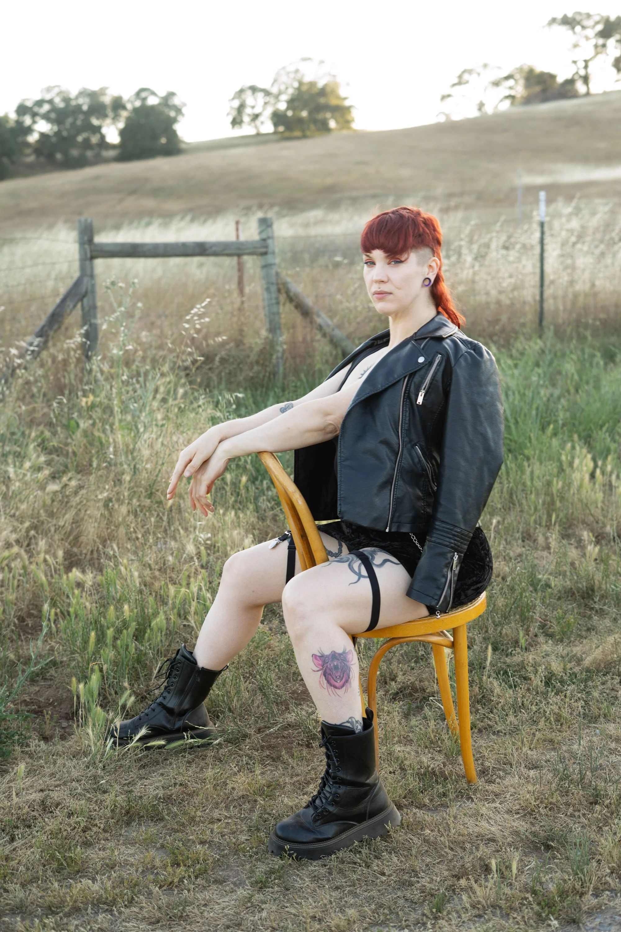 red haired woman sitting on yellow chair in grassy field with fence in background