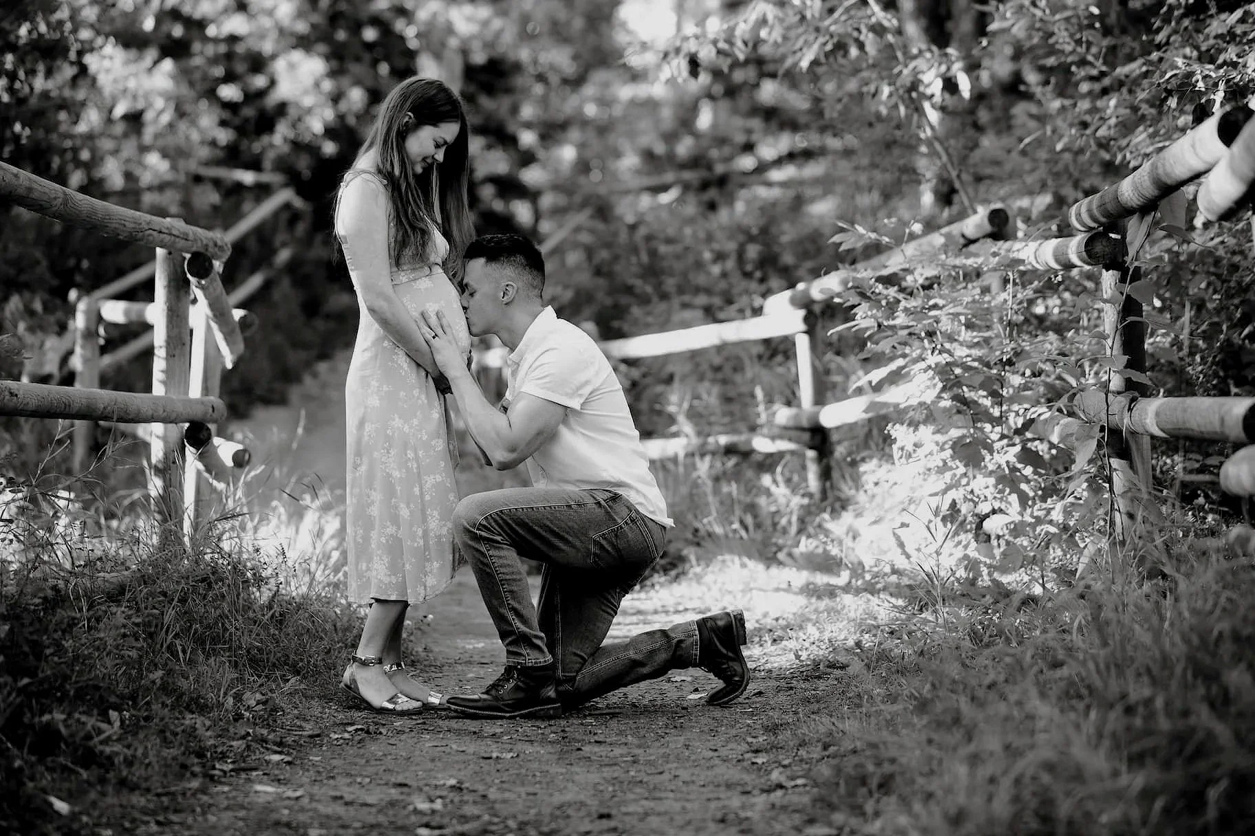 calgary maternity photo in a park of husband kneeling to kiss his wife's belly