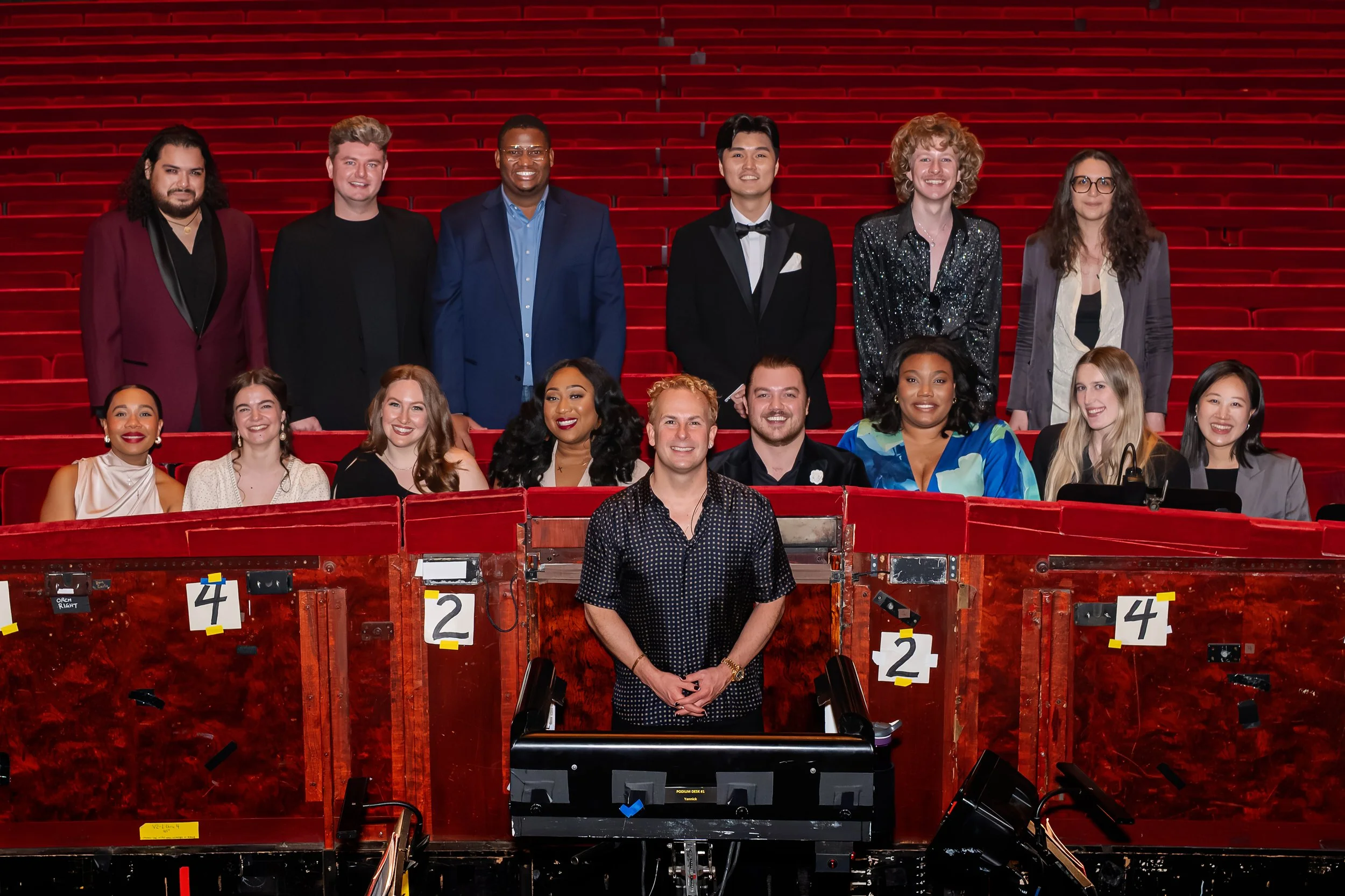 Group of 16 diverse people posing in a theater with red seats for a photo.