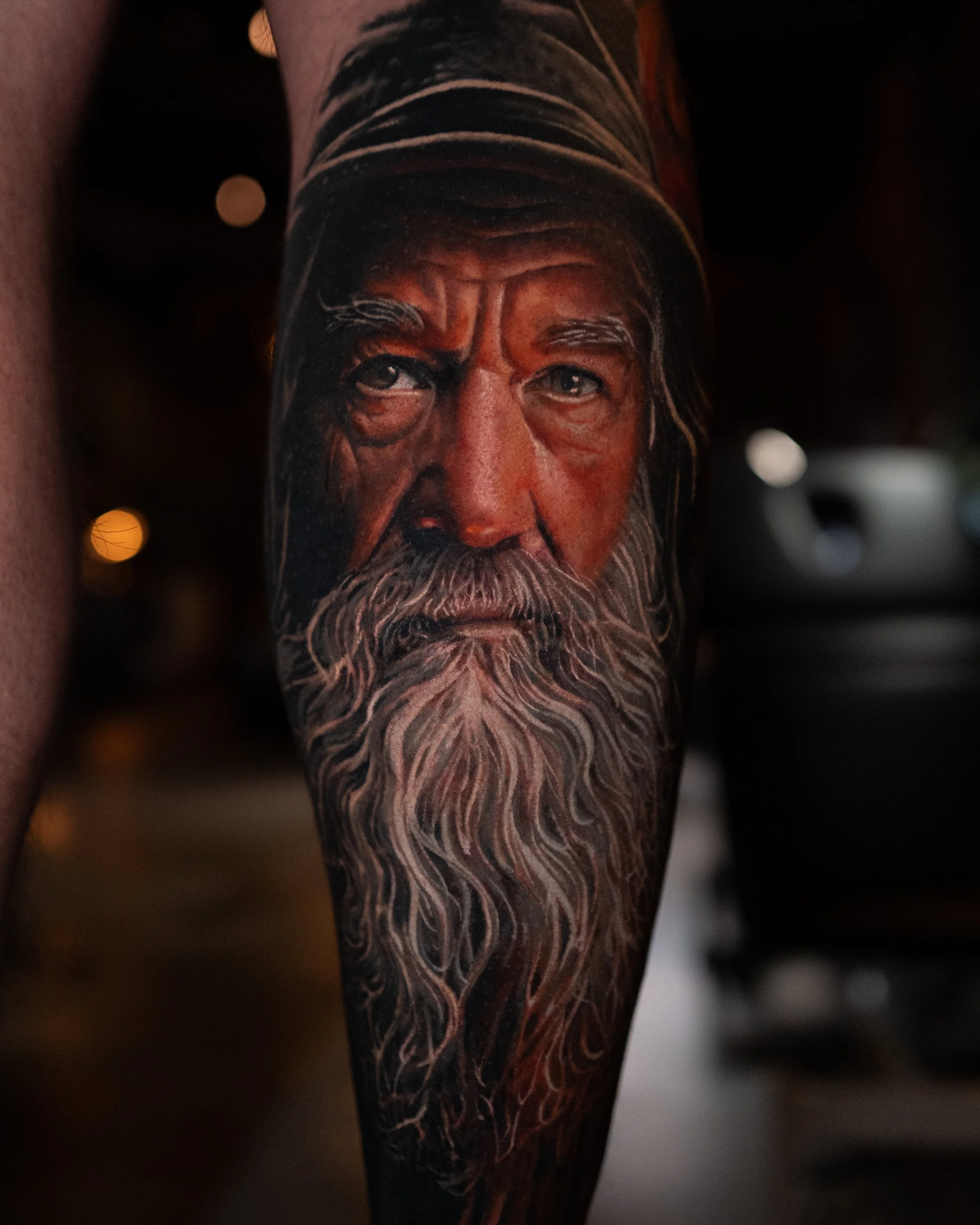 A detailed tattoo of an elderly man's face with a long, flowing white beard on a person's arm.