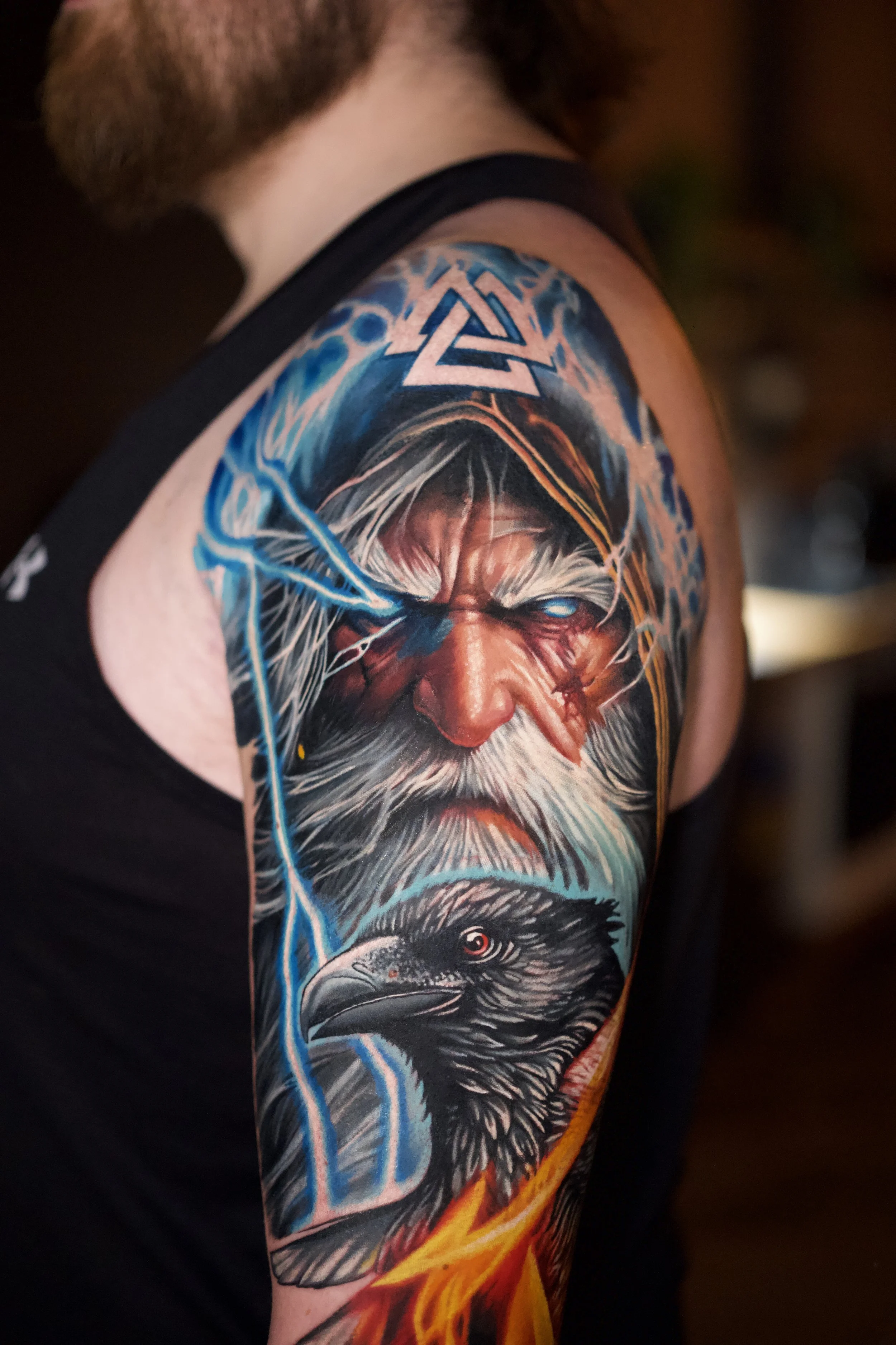 Colorful tattoo of a wizard with a long beard and glowing eyes, and an eagle with a fiery background and lightning elements.