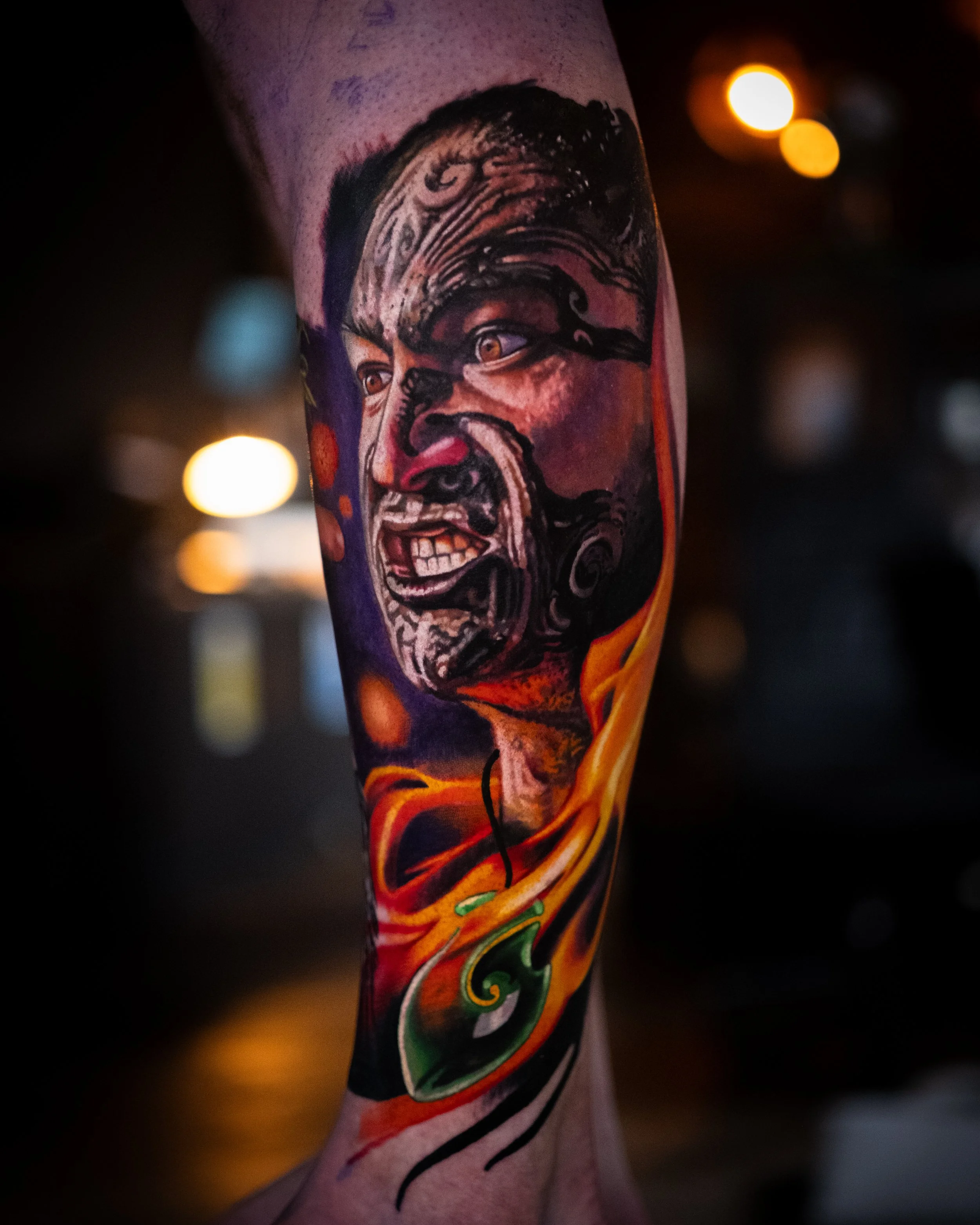 Colorful tattoo of an angry face with bulging eyes, clenched teeth, and intricate details, with swirling flames or smoke around the neck area.