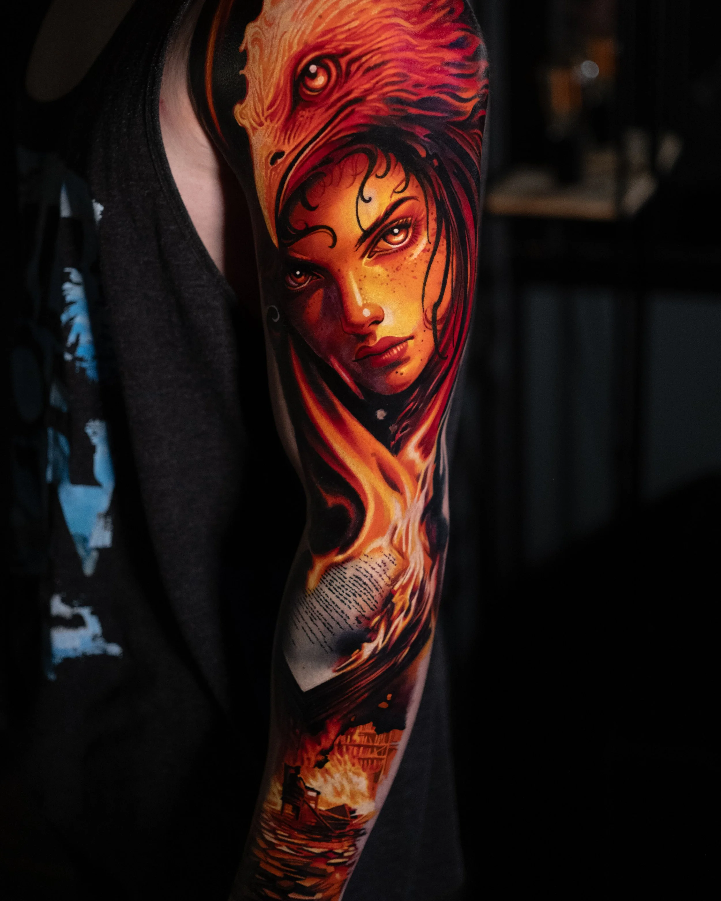 Colorful tattoo of a woman's face with long flowing hair, set against a fiery background with flames and a boat on water.