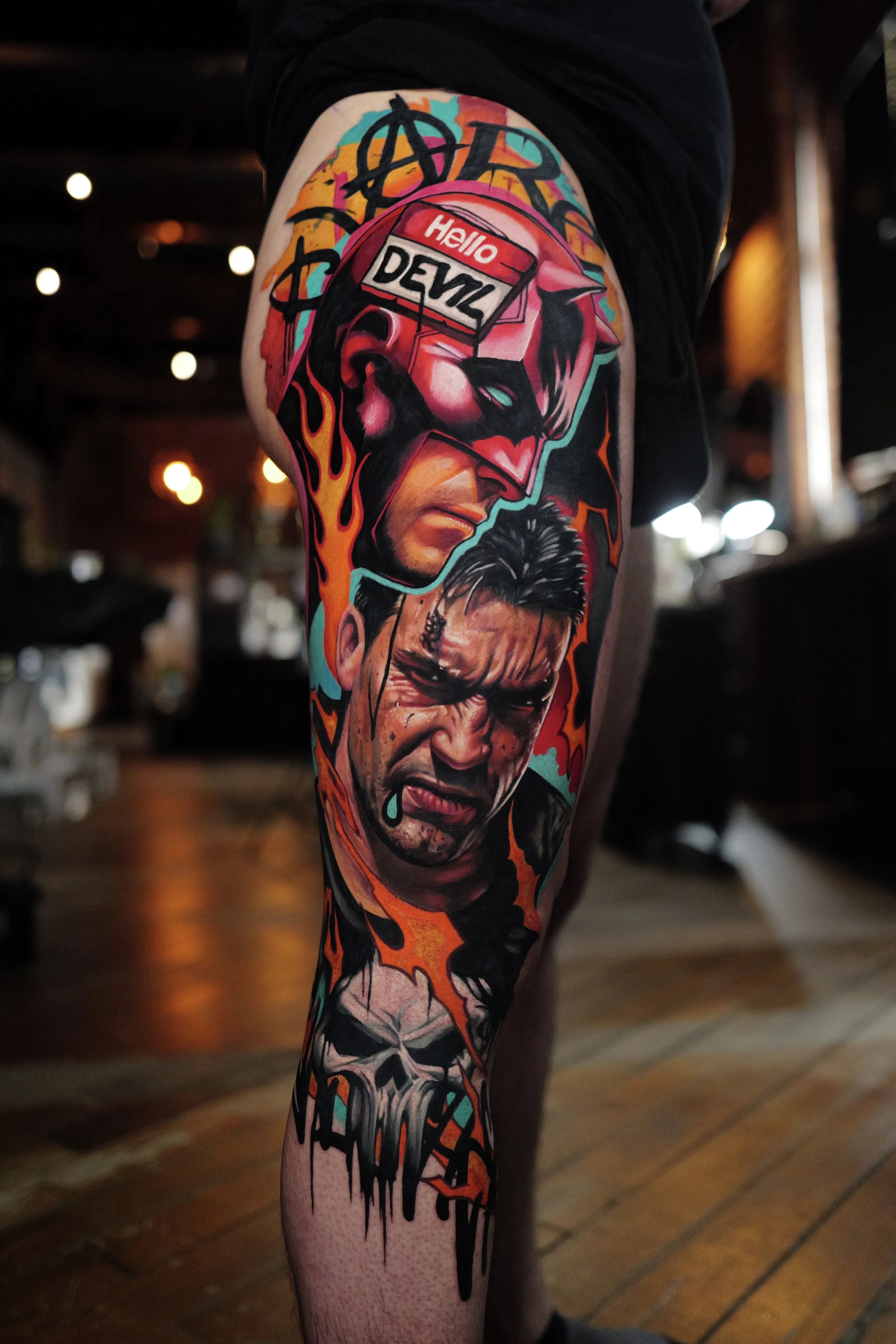 Colorful tattoo sleeve depicting a masked figure with a 'Hello Devlz' sign, an angry face with a tear, and a skull, with flames and abstract designs.
