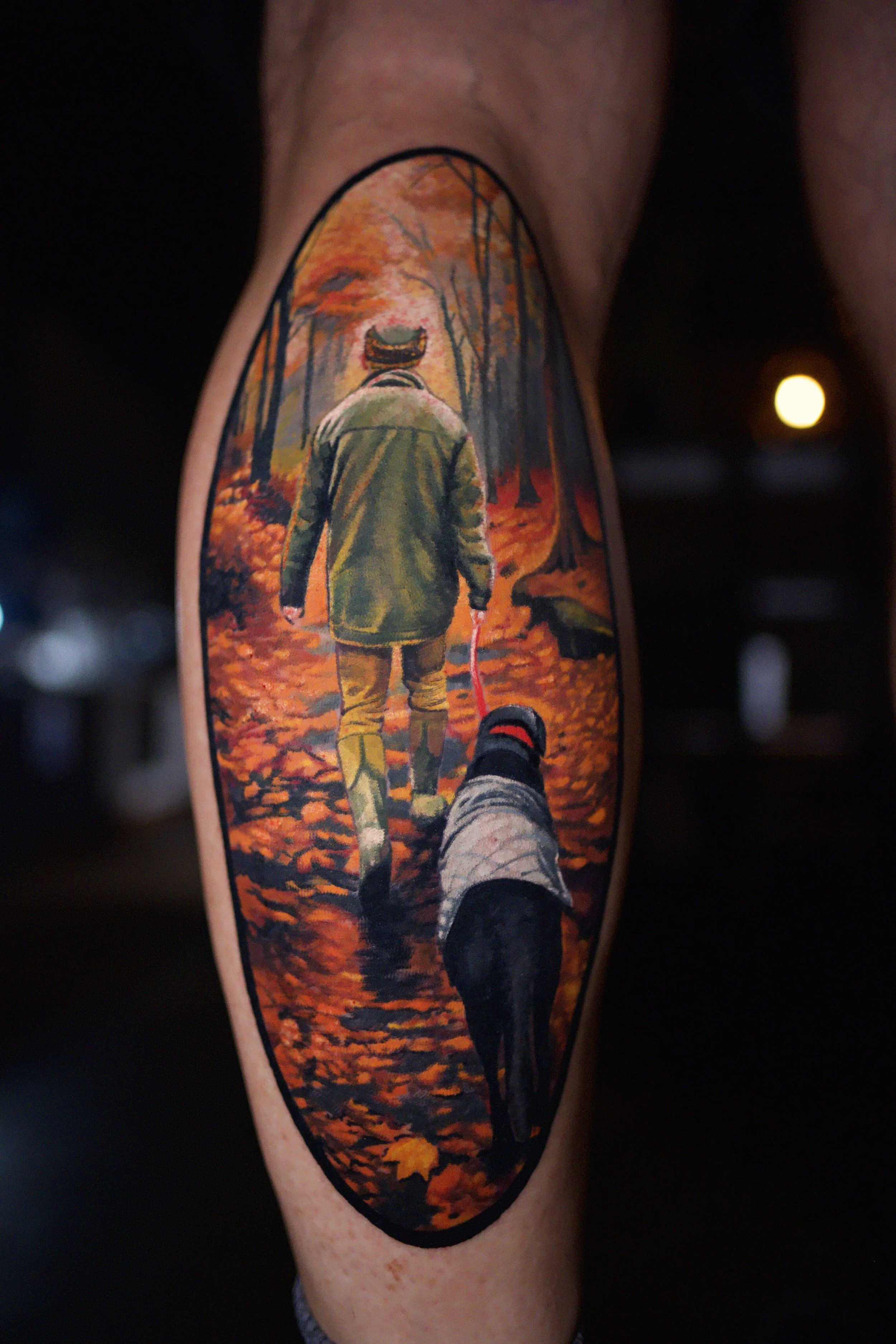 Tattoo of a person walking a dog through an autumn forest with fall leaves on the ground.