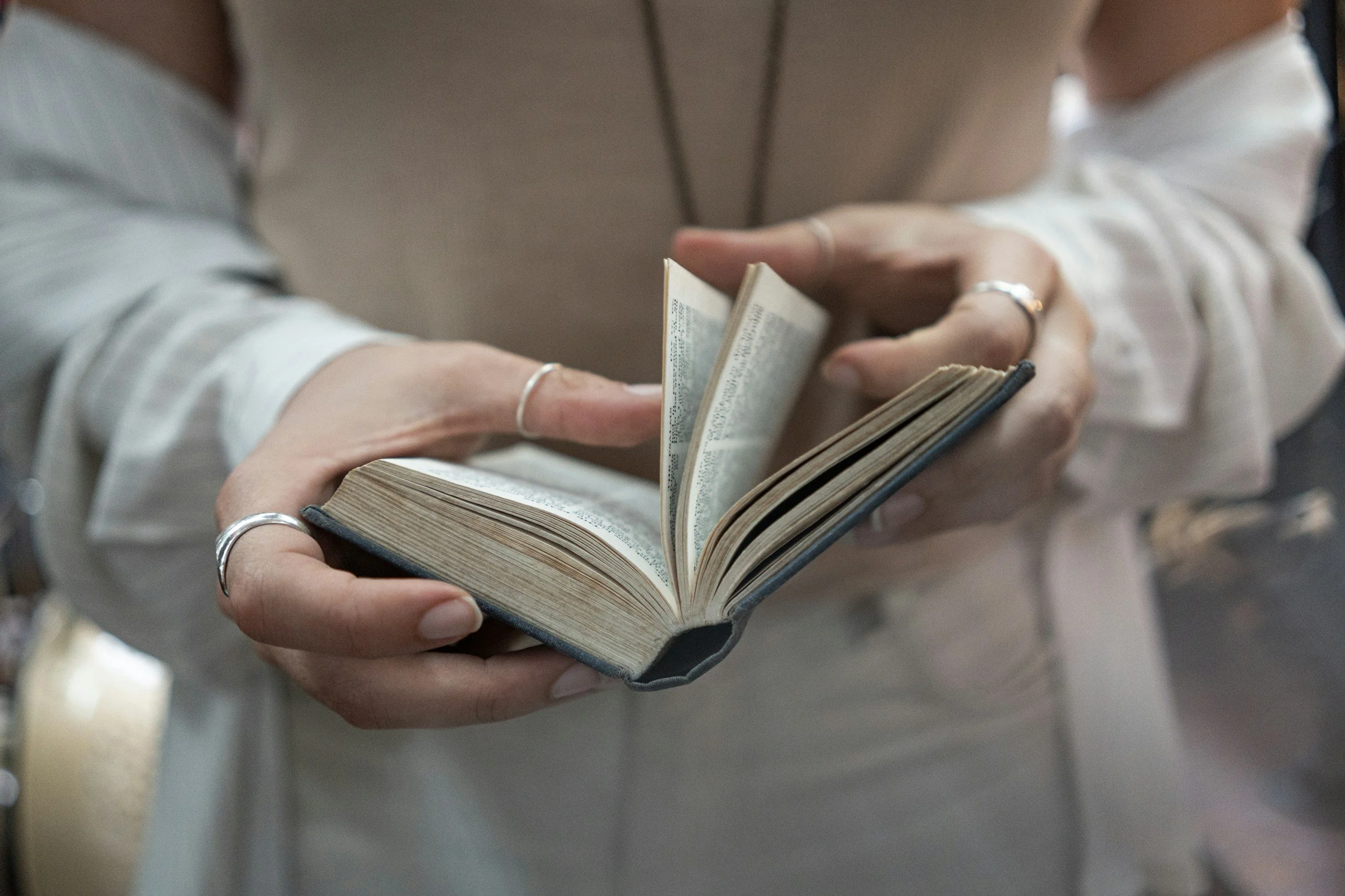 A person holding and flipping through a small, slightly worn book or notebook with handwritten text, wearing a silver ring on their fingers.