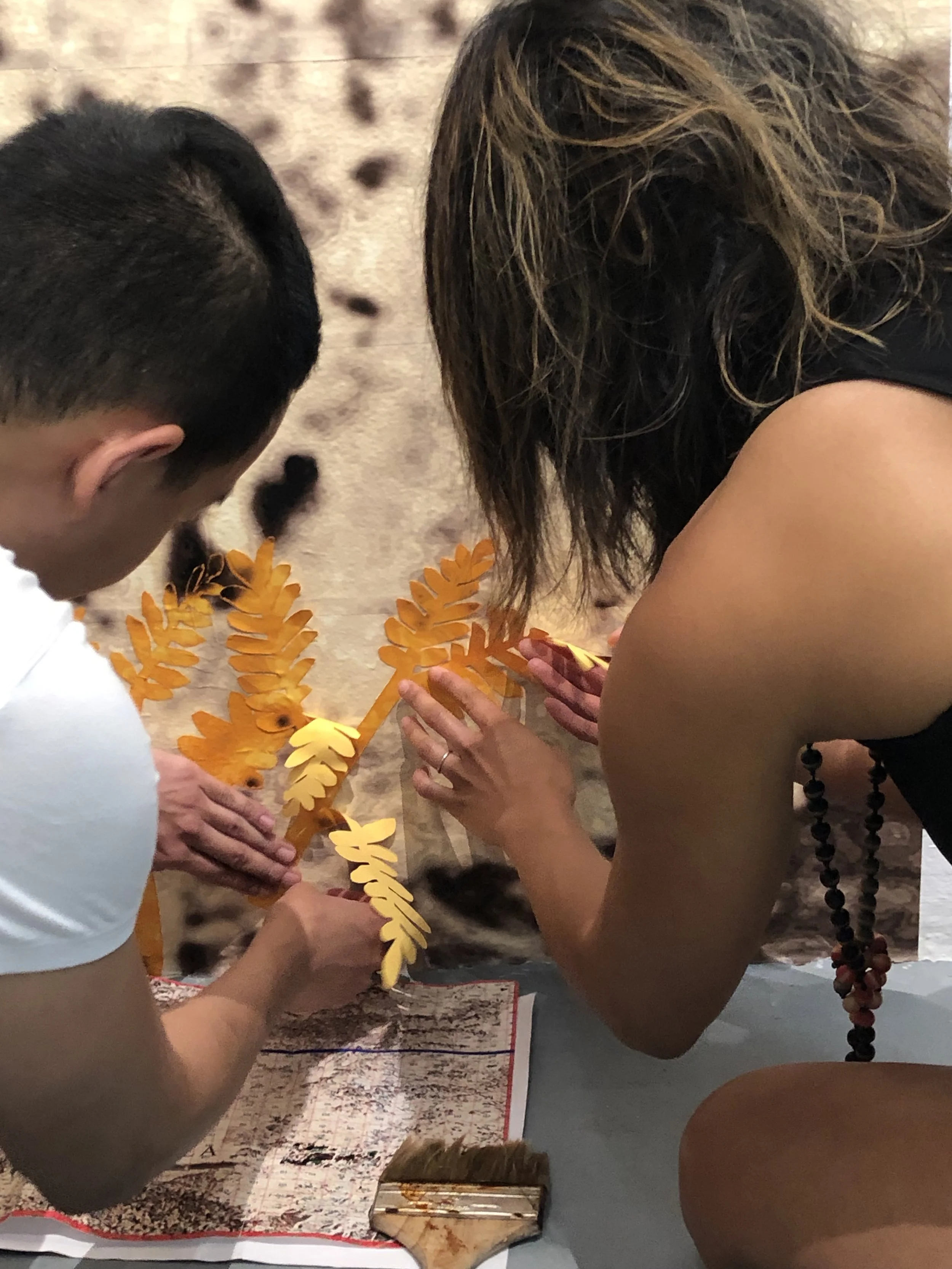 Hand cut Sunshine Wattle overlay being aligned and affixed by a member of the Bondi and Tamarama Costal Bush Regeneration Collective