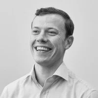 A smiling man with short hair wearing a collared shirt.