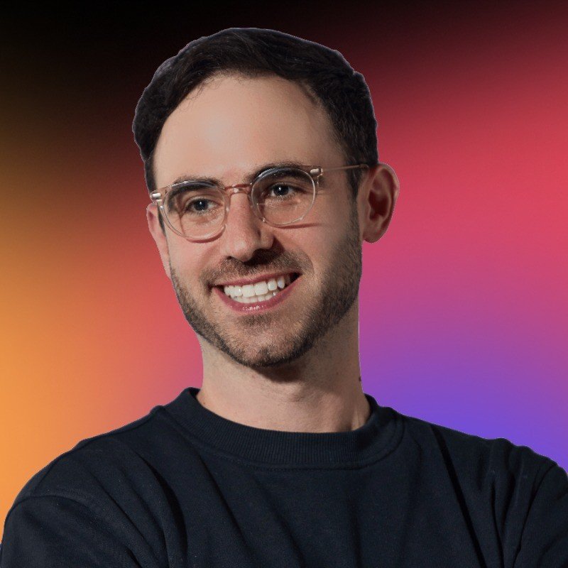 A young man with glasses smiling against a vibrant, multi-colored background.