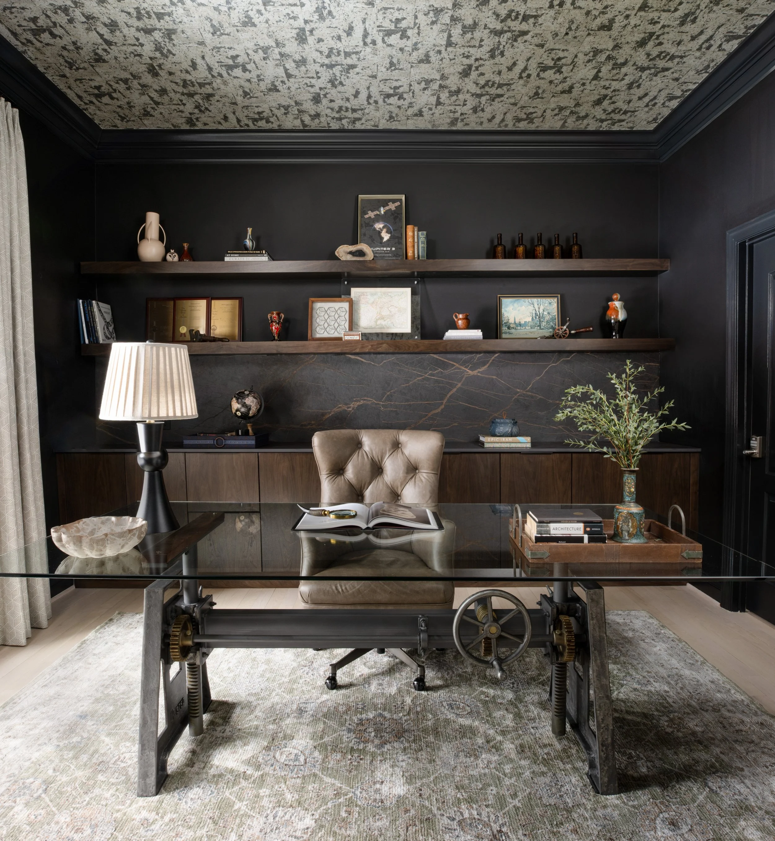 Luxury home office design by House of Shima featuring Benjamin Moore Onyx walls, custom walnut shelving, decorative ceiling wallcovering, vintage furnishings, and carefully curated accessories.
