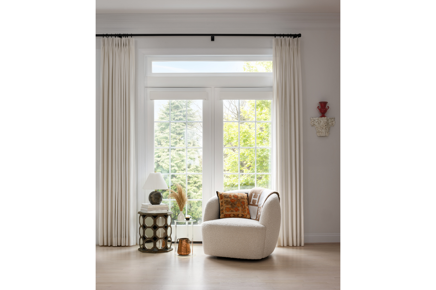 Custom window treatments framing a bright living room with tailored drapery, a boucle accent chair, and layered furnishings designed for a timeless, personalized home.