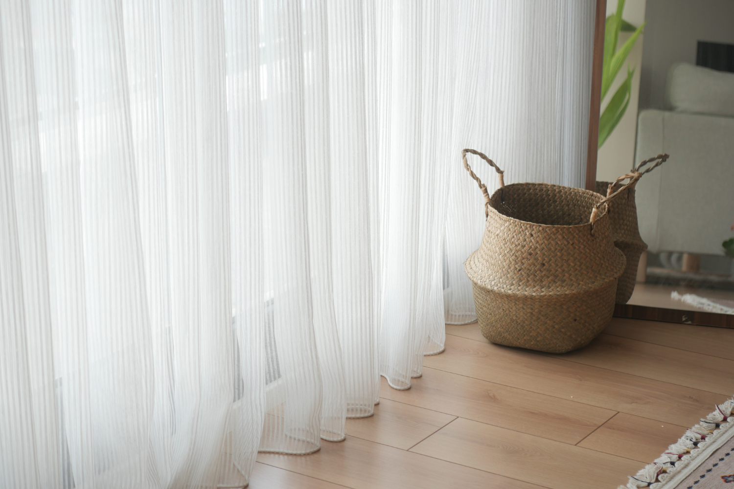 Sheer white drapery styled with woven natural textures and warm wood flooring, creating a bright and airy summer-inspired interior atmosphere