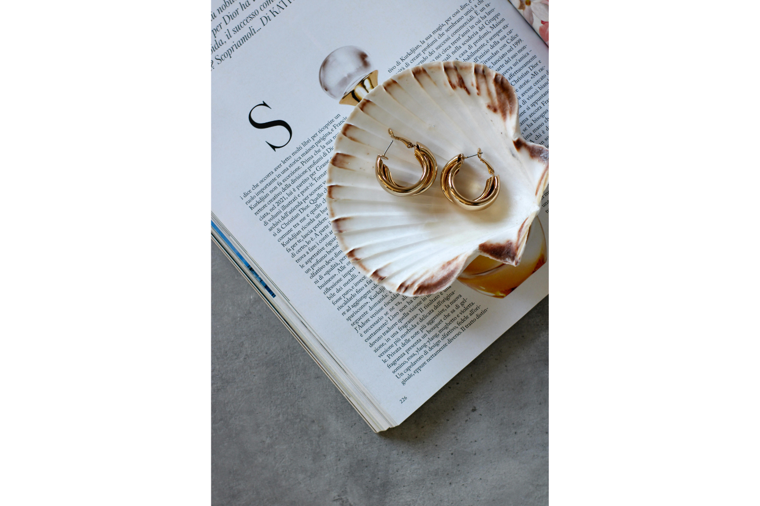 oastal-inspired summer interior styling featuring a decorative seashell dish, gold jewelry, layered textures, and soft neutral tones styled over an open magazine.