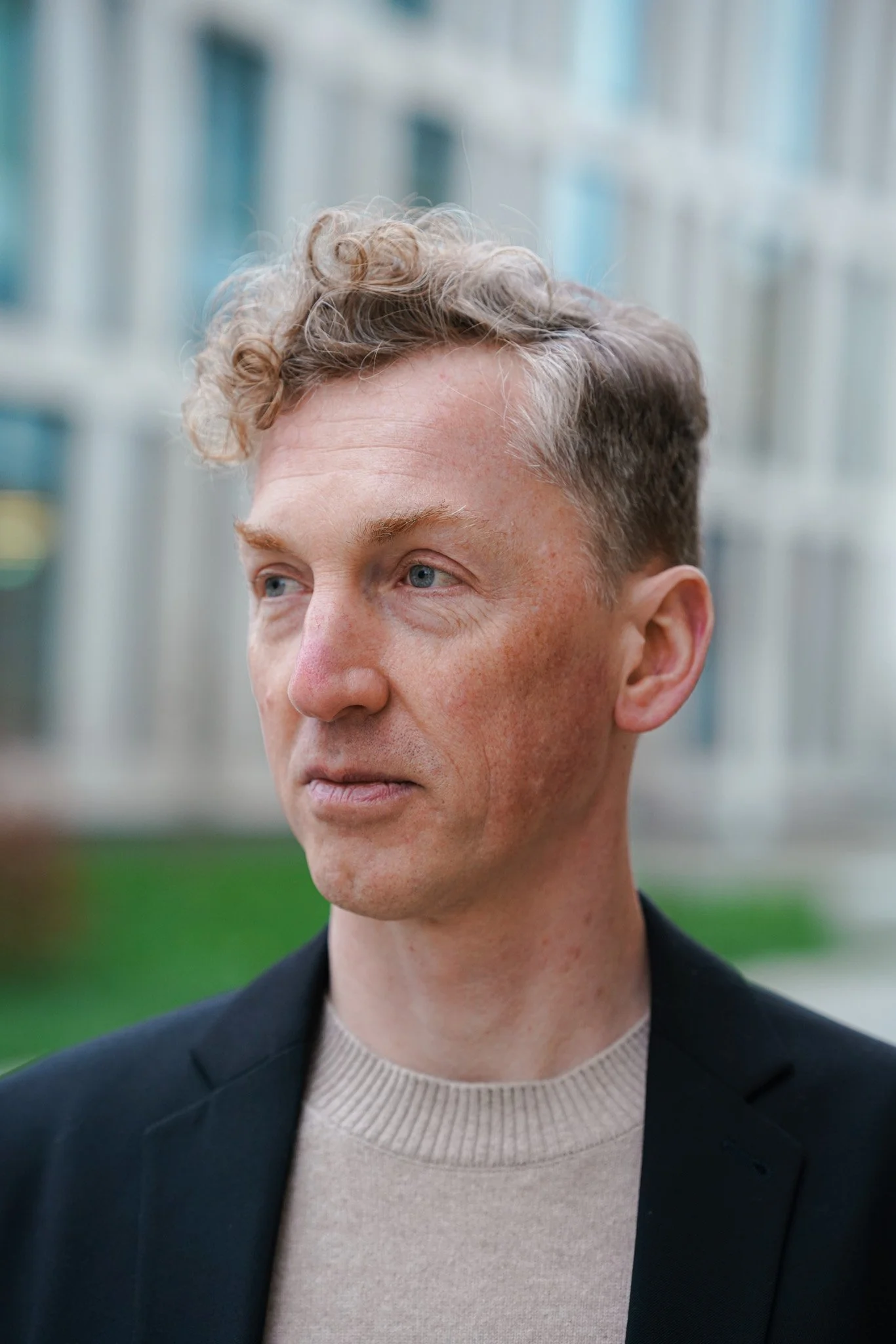 Nahaufnahme von Marcel Krüger, Philosoph, im Vordergrund, im Hintergrund ein moderner Gebäudekomplex mit Glasfenstern