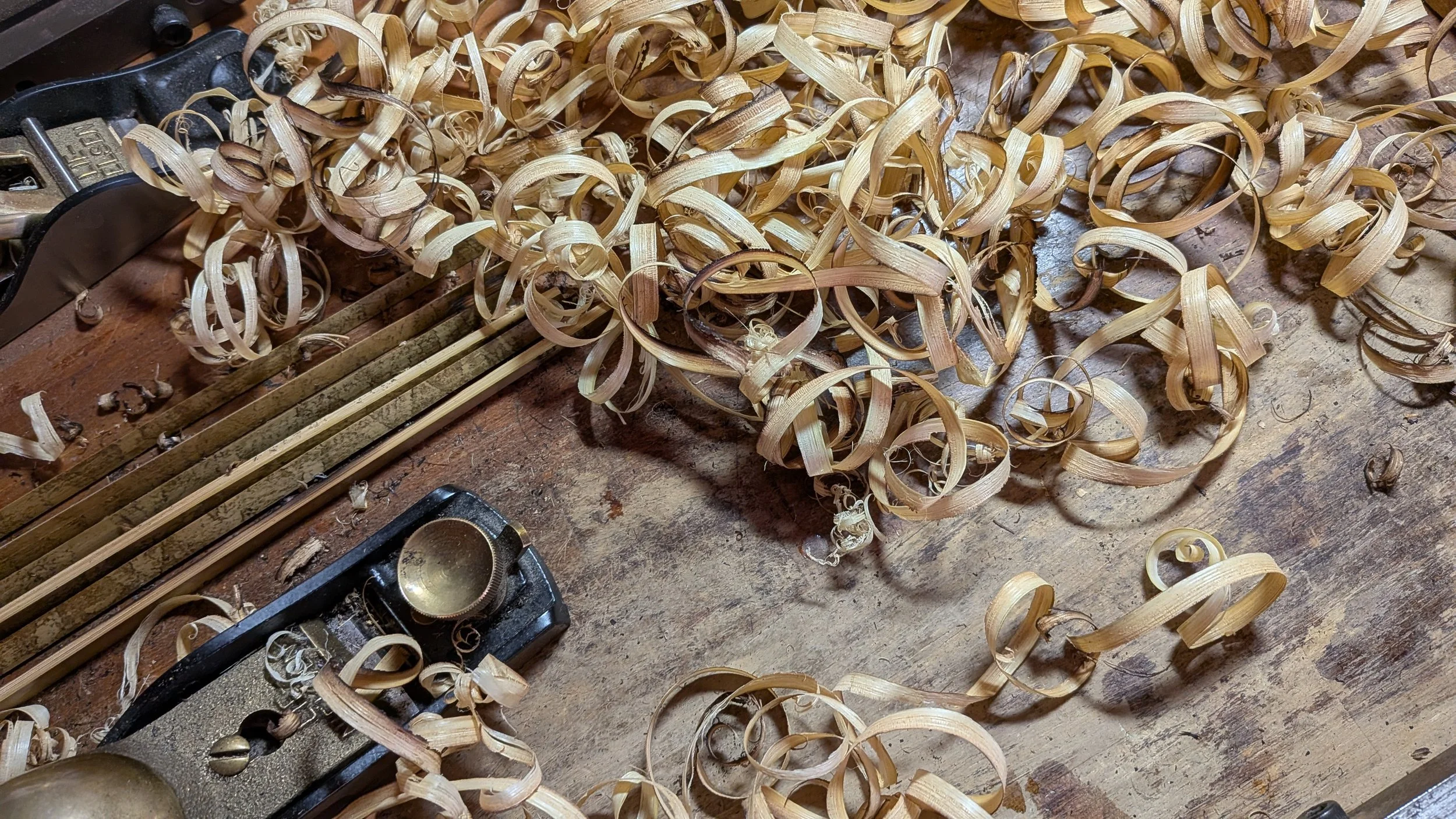 Wood shavings on a workbench with tools nearby, including a vibrating tamper and a digital scale.
