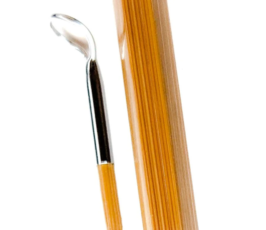 A metal dental scaler with a pointed curved tip positioned next to a wooden toothpick.