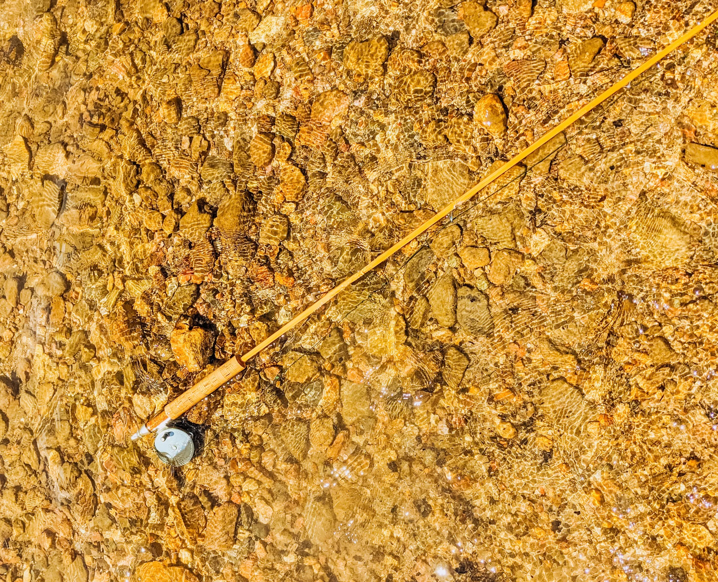 A fishing rod and a can placed on a large rock with a textured, layered surface.