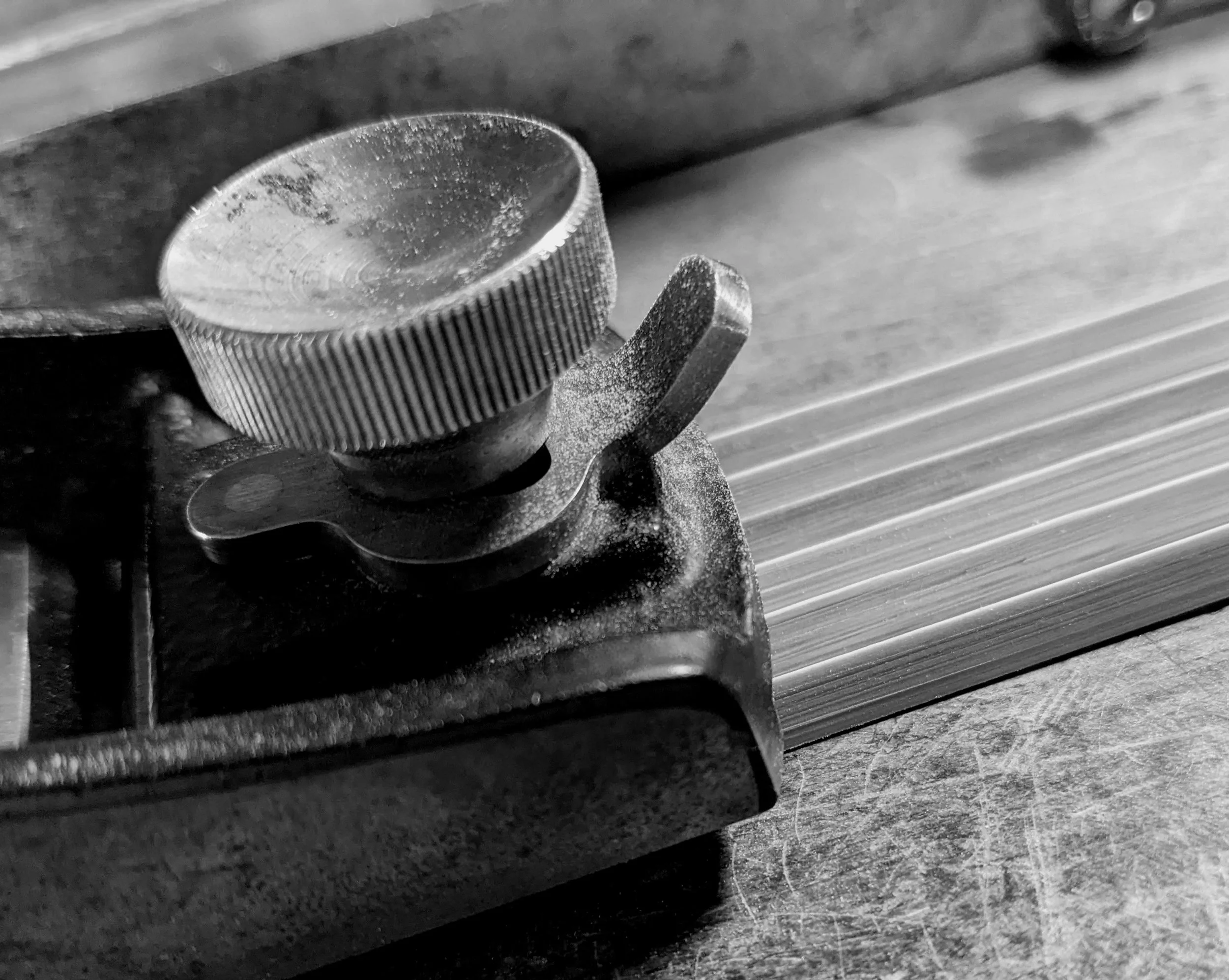 Close-up of a metallic gear or knob with ridged edges, mounted on a machine, with a textured surface and a grid-like pattern in the background.