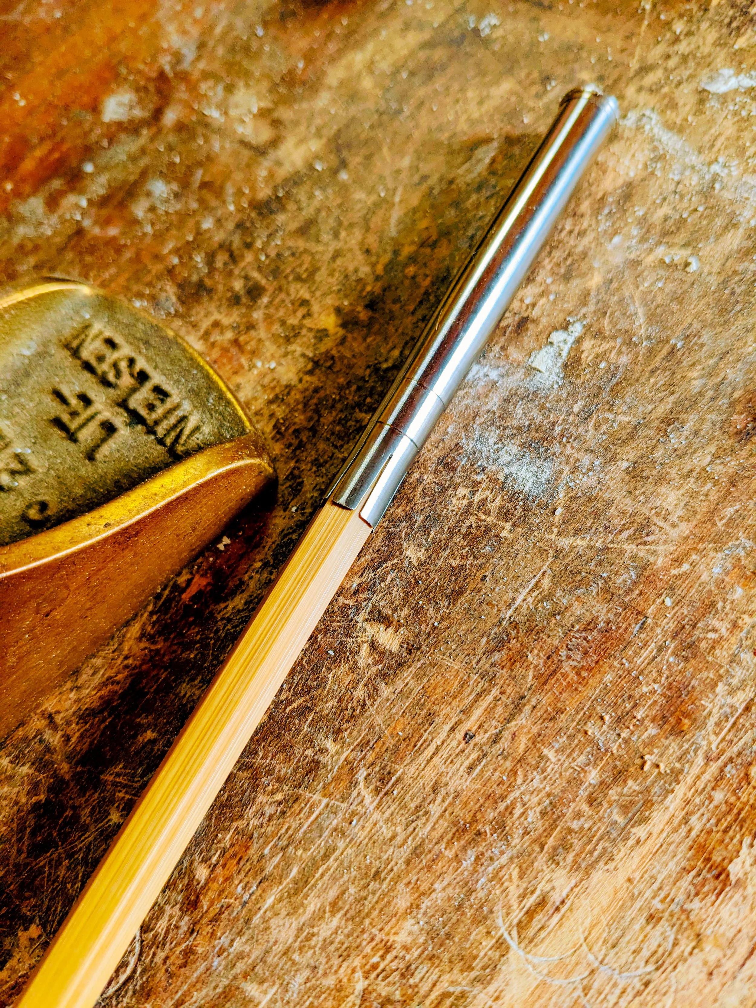 A close-up photograph of a metallic pen lying on a textured wooden surface, with a cork object partially visible on the left side.