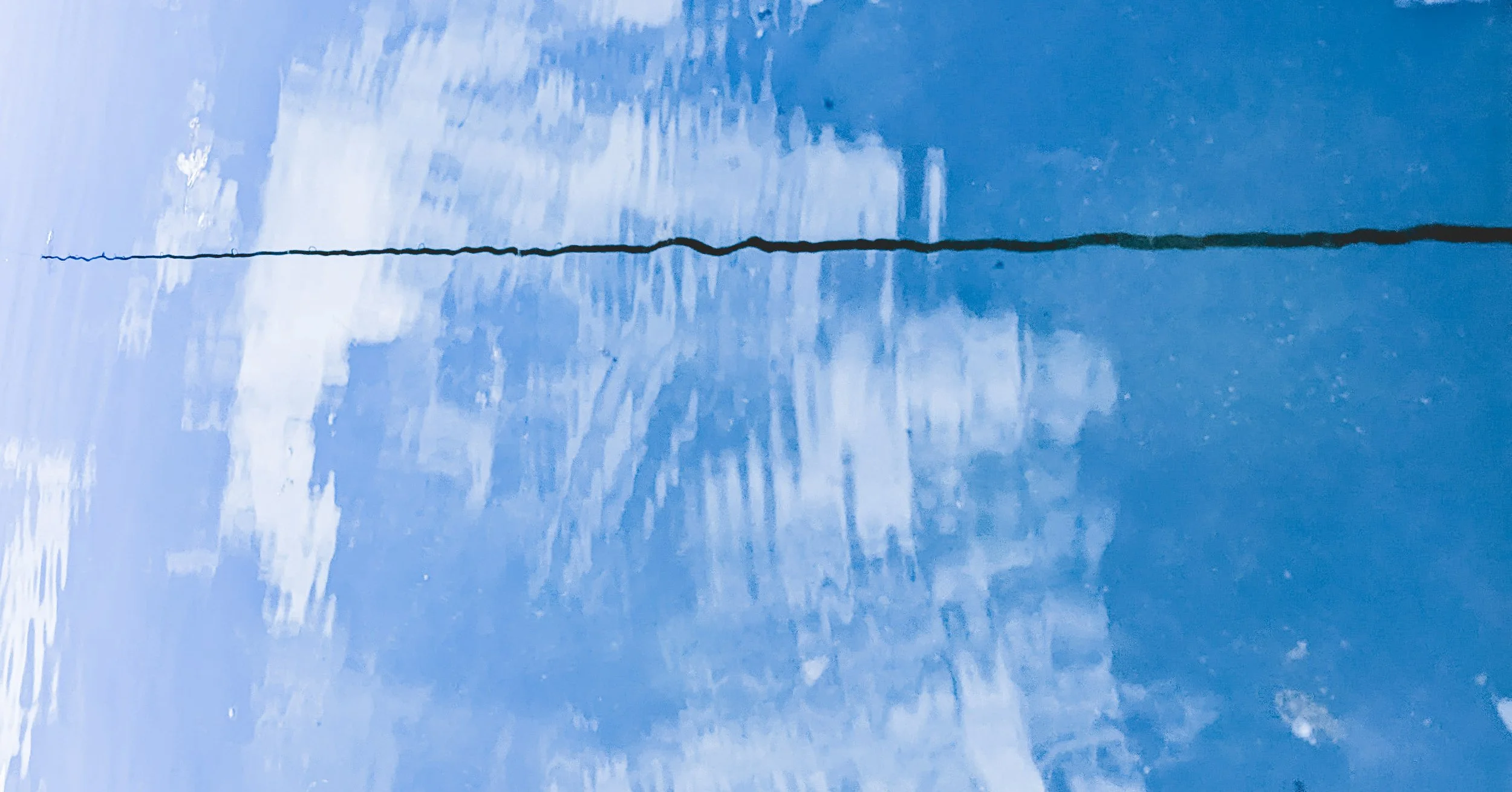A blue surface reflecting the clouds and sky above, with a black line running horizontally across the middle of the image.