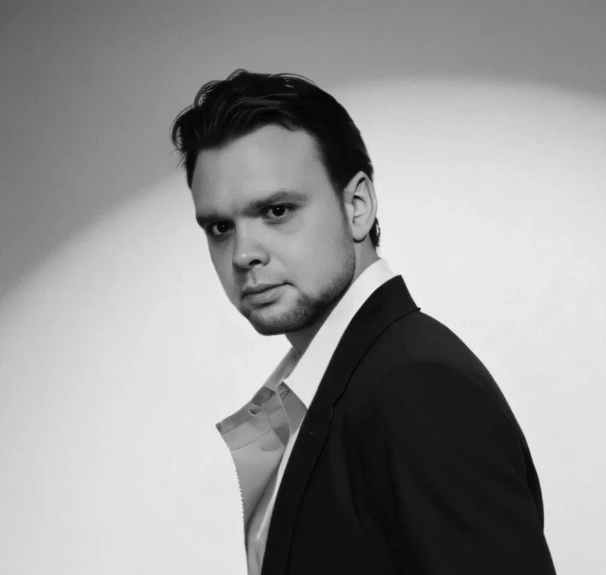 A black and white portrait of a man in a suit looking directly at the camera.