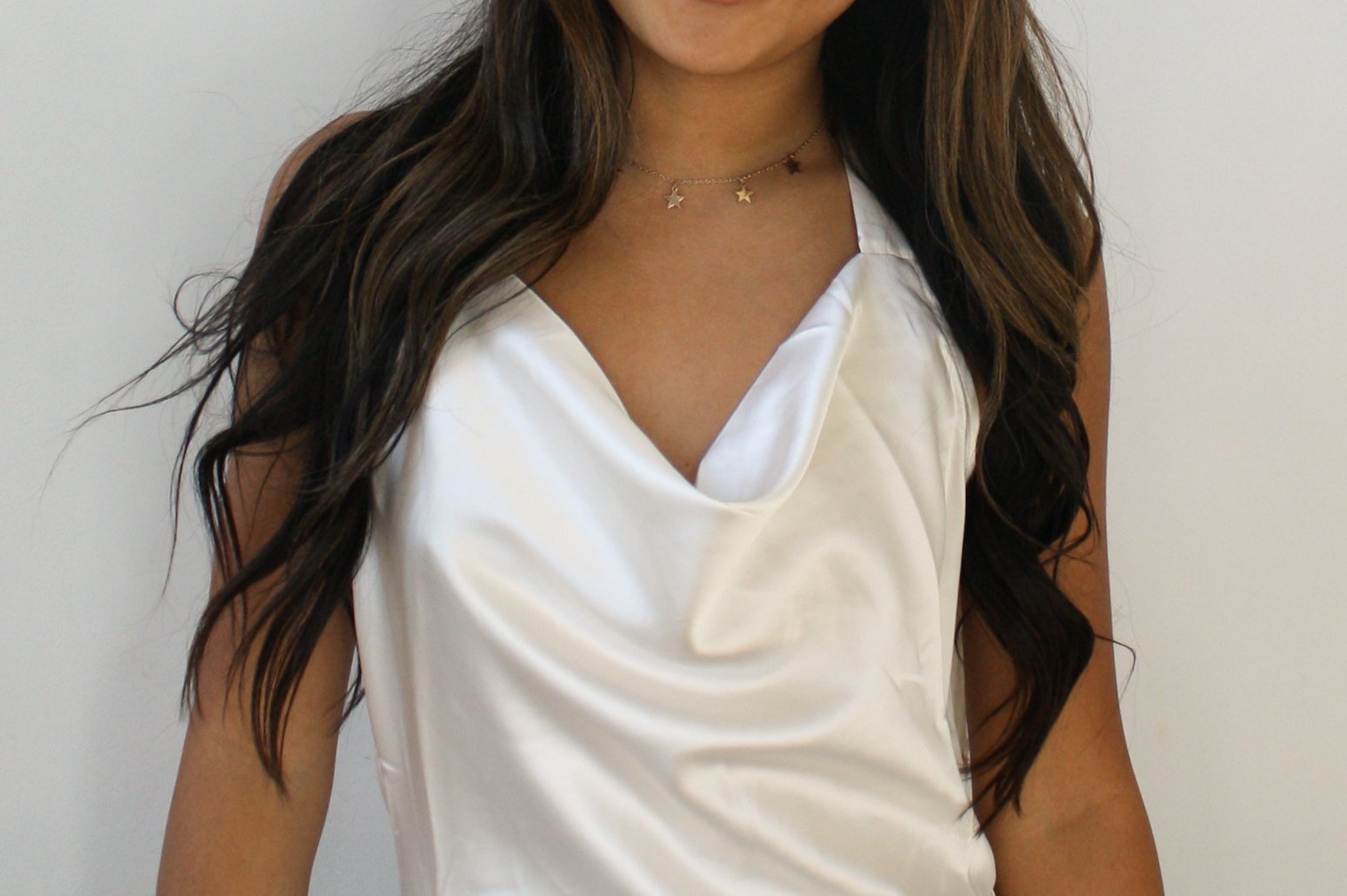 A woman wearing a white satin sleeveless top and a necklace with star-shaped charms.