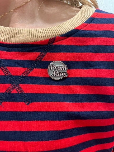 Person wearing a striped red and navy shirt with a beige collar and a 'Prom Mom' pin.