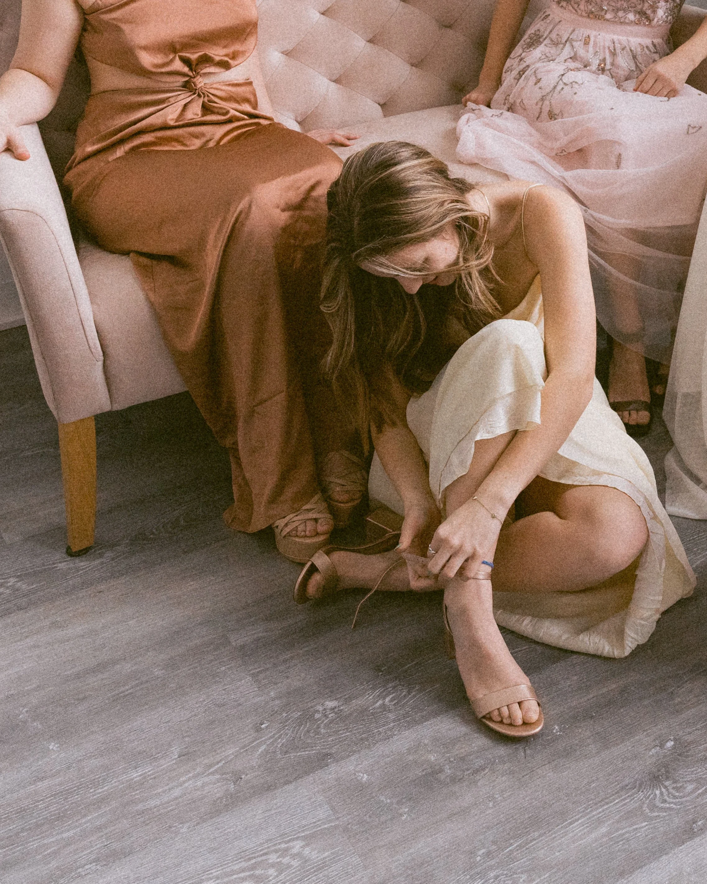 A woman sitting on the floor helping another woman put on a dress shoe.