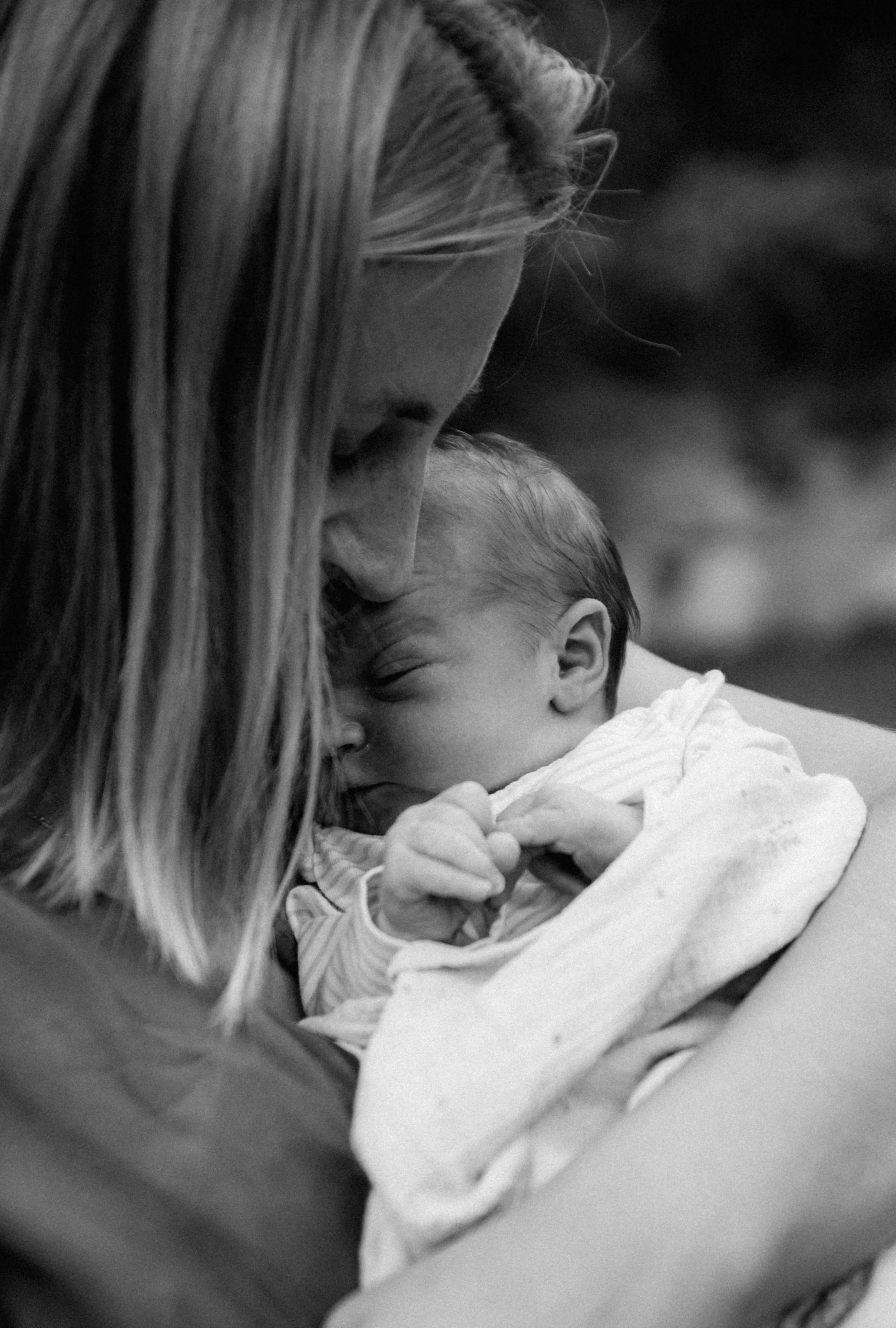 Černobílá fotografie ženy, která drží spící novorozené miminko blízko svého obličeje, jejich hlavy se jemně dotýkají. portrétní fotografie. newborn