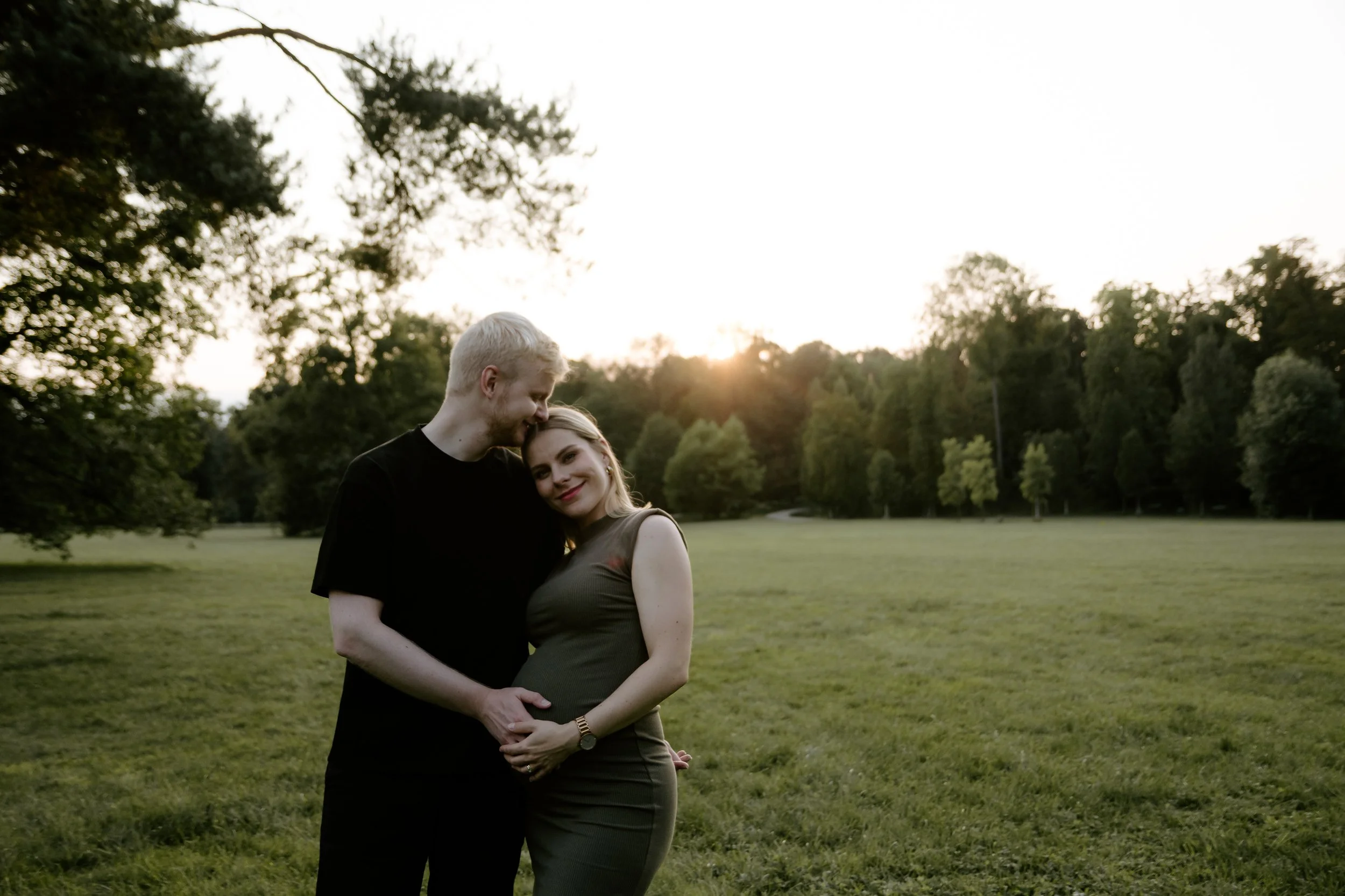 Pár stojí blízko u sebe v parku při západu slunce, v pozadí stromy a tráva. portrétní fotografie.