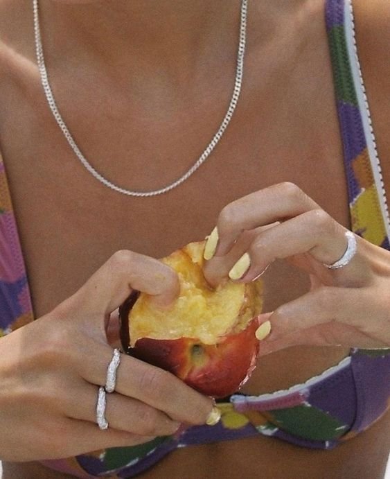 Person peeling and eating an apple, wearing jewelry, and a colorful top.