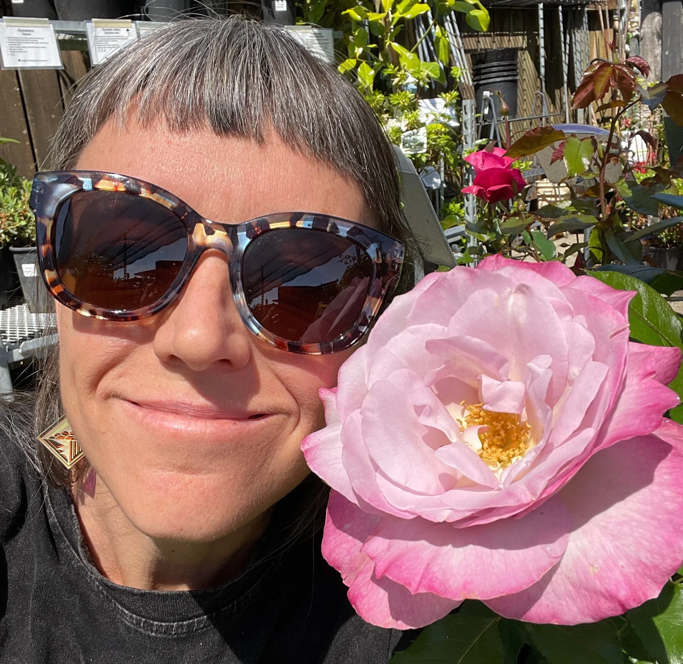 Rev. Cindy with giant pink rose next to face smiling into sun