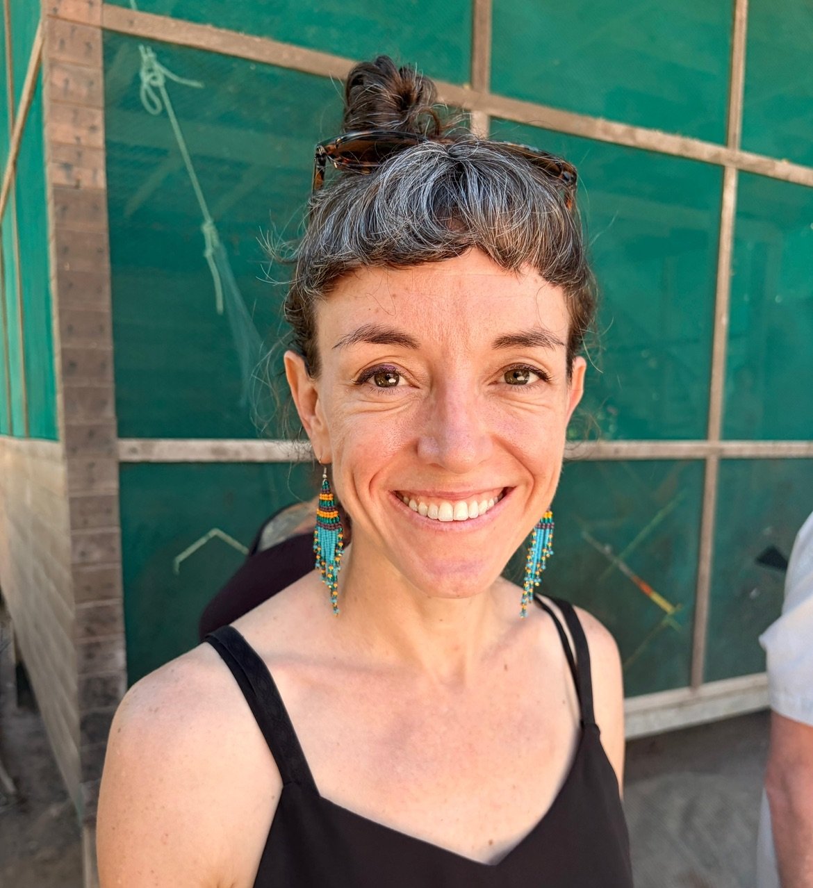 Rev. CIndy Pincus standing in front of house smiling with green earrings and black tanktop